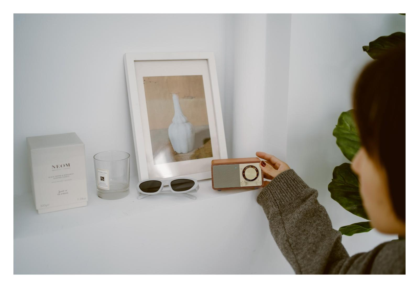 Eine Hand berührt ein Holzradio auf einem Regal neben einem Bild und einem Glas.