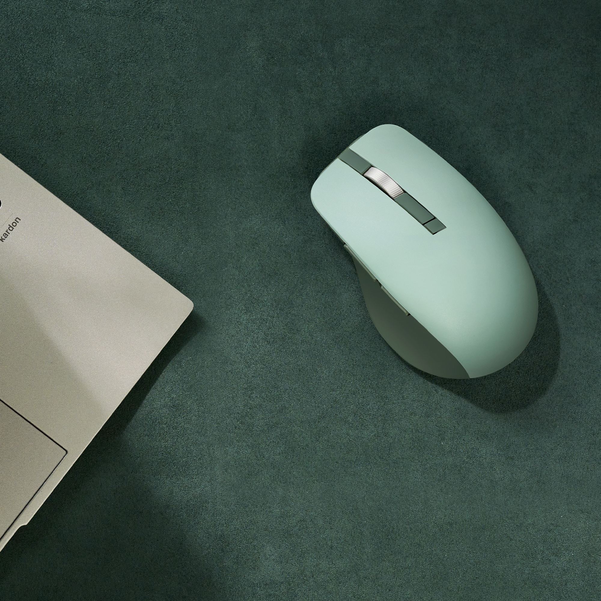 Un mouse del computer verde menta e parte di un laptop su sfondo verde scuro.