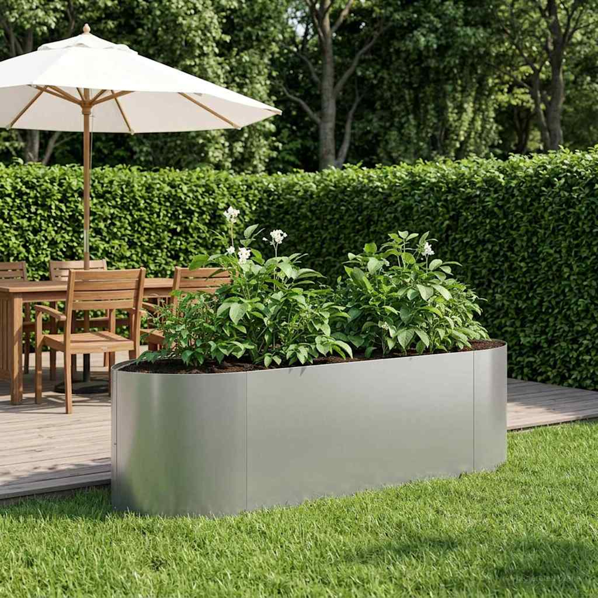Ein rechteckiger Hochbeet aus Metall mit grünen Pflanzen steht auf einer Holzterrasse neben einem Esstisch.