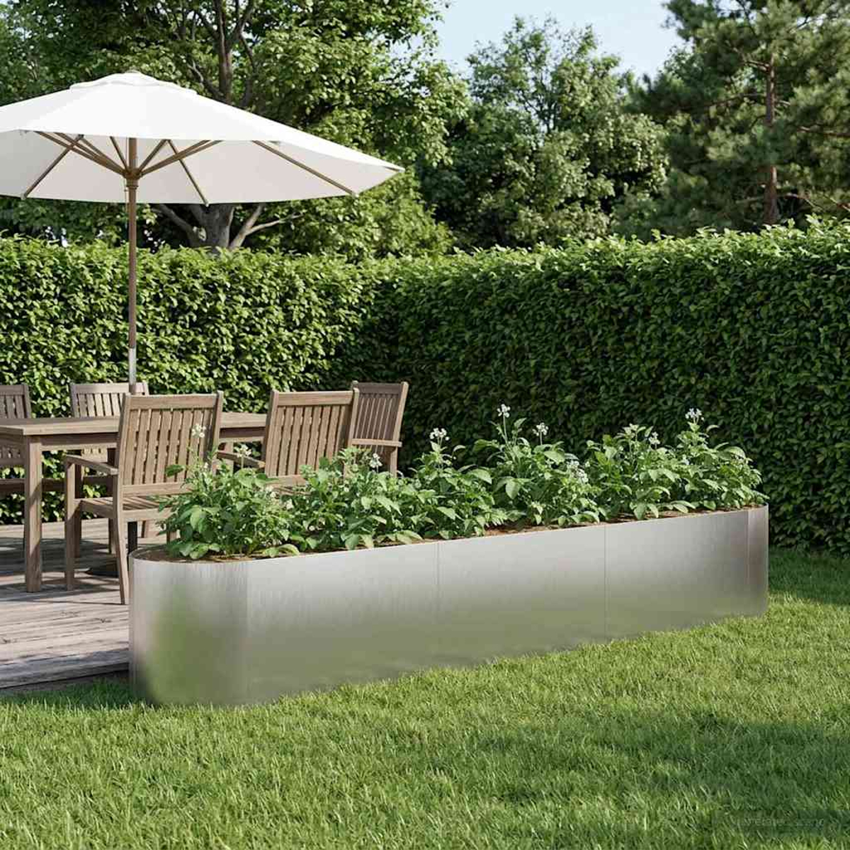 Ein Metallpflanzer mit grünen Pflanzen steht auf Gras neben einem Holztisch und Stühlen unter einem Sonnenschirm.