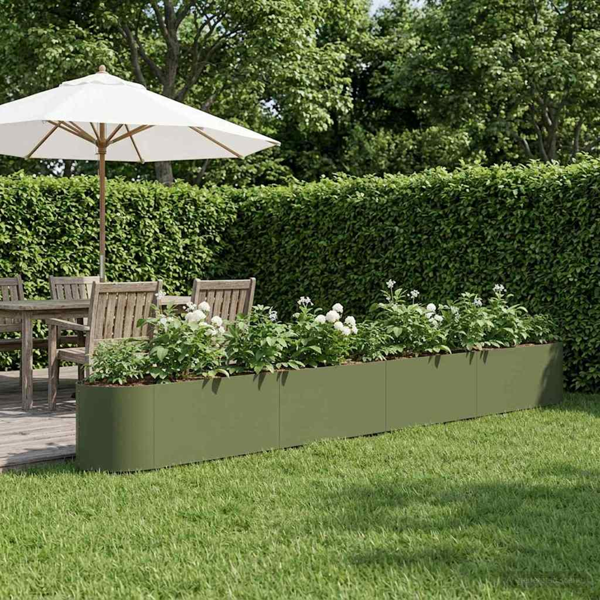 Ein grüner Pflanzer mit weißen Blumen steht auf saftigem Gras neben einem Holztisch.
