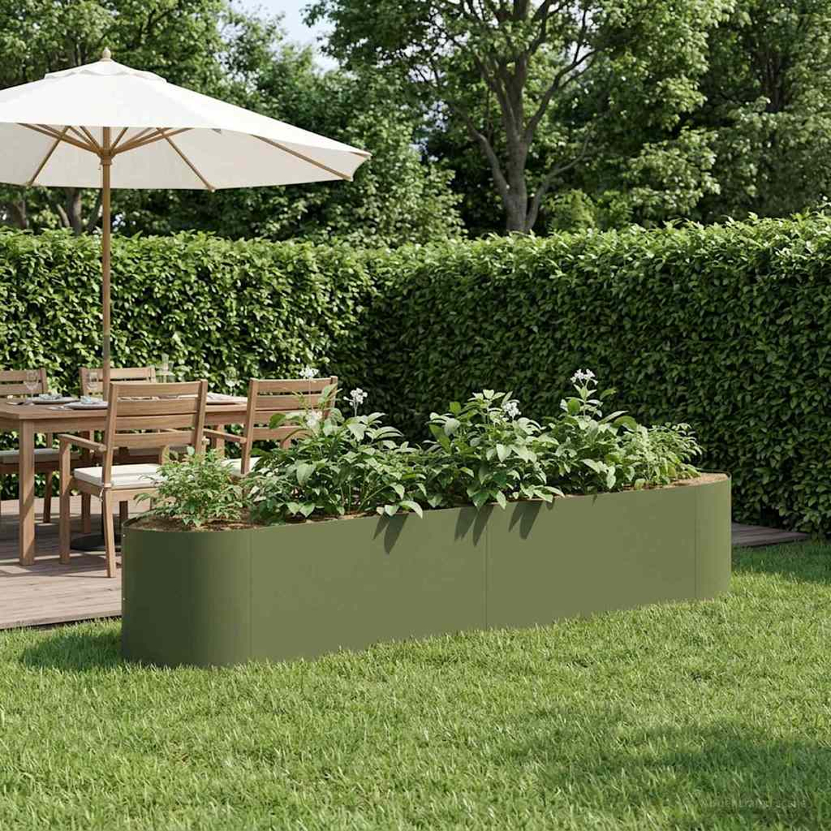 Ein grünes Hochbeet mit Pflanzen steht auf Rasen vor einer Hecke. Ein Tisch und Stühle sind im Hintergrund.