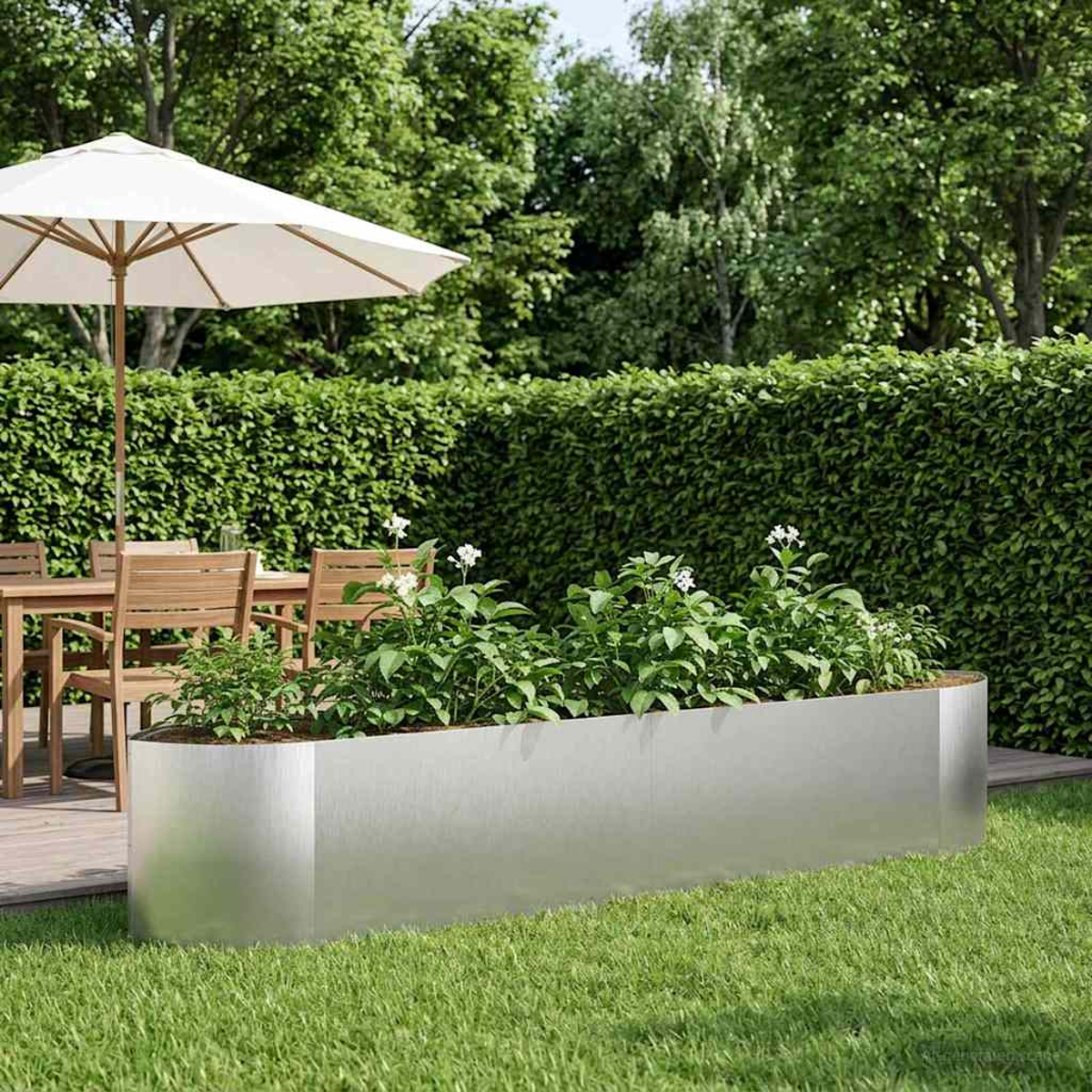 Ein moderner rechteckiger Hochbeet aus Metall steht im Gras vor einer Hecke.