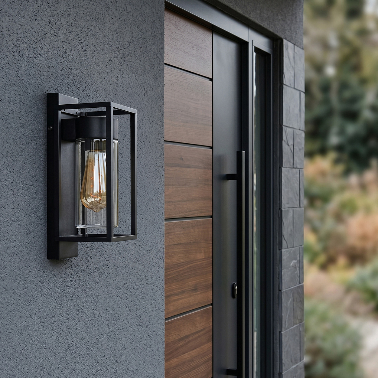 Moderne Wandleuchte mit Glaszylinder und Glühbirne an einer grauen Wand neben einer Holztür.