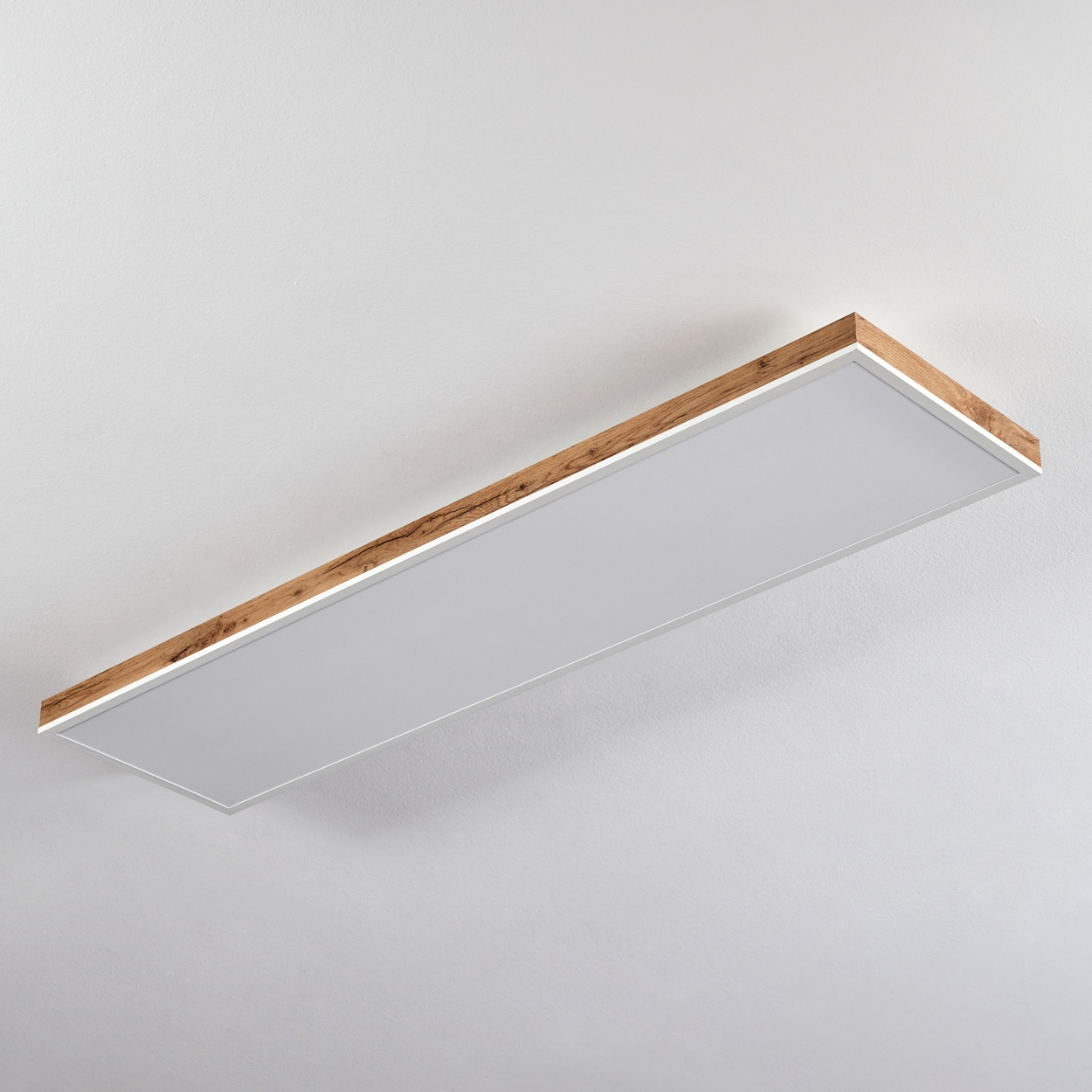 Eine rechteckige Deckenleuchte mit Holzrand und weißem Diffusor hängt an einer weißen Decke.