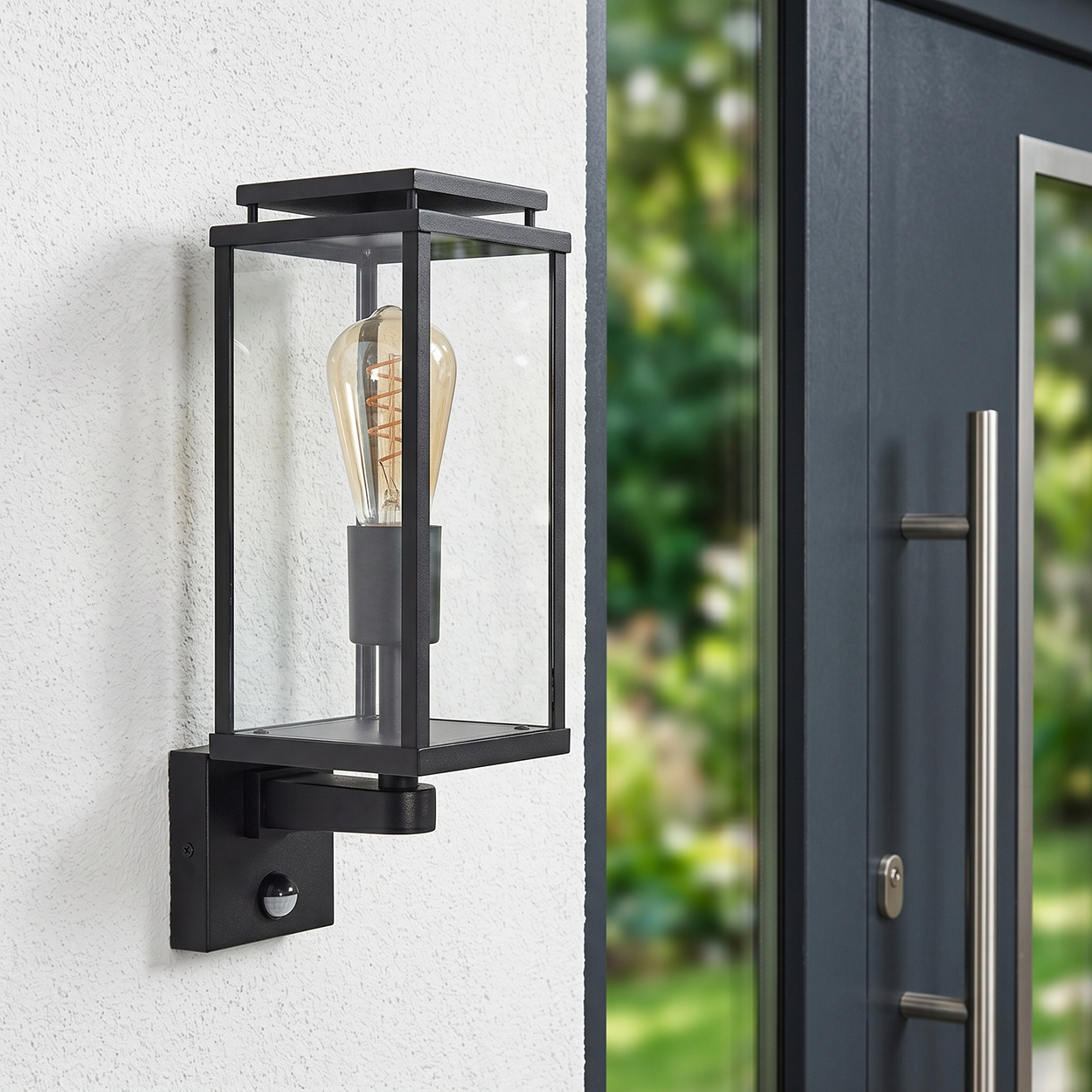 Schwarze Wandleuchte mit Glas und Glühbirne neben dunkler Tür.