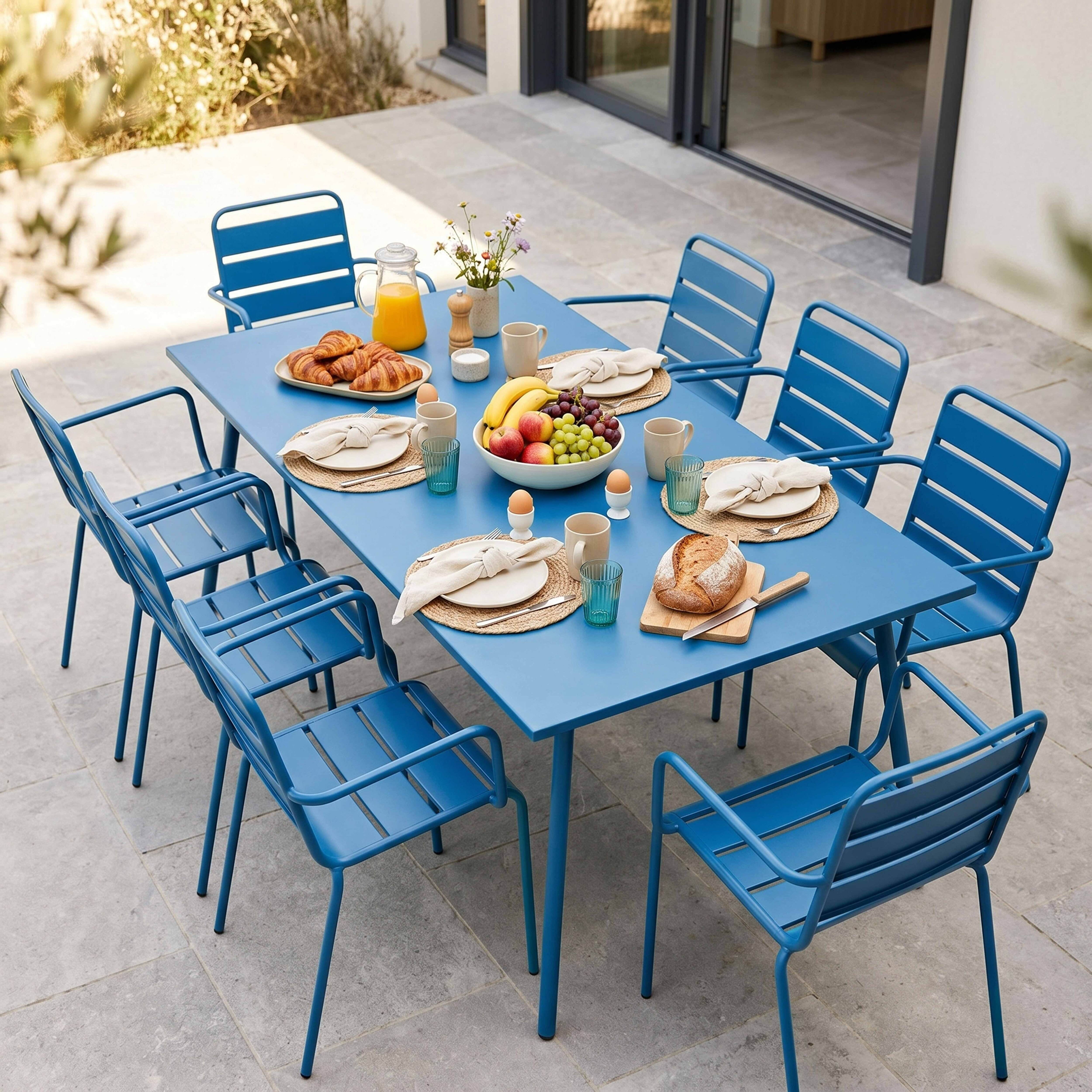 Ein blaues Esszimmerset für draußen mit sechs Stühlen, beladen mit Frühstücksartikeln wie Obst, Croissants und Saft.