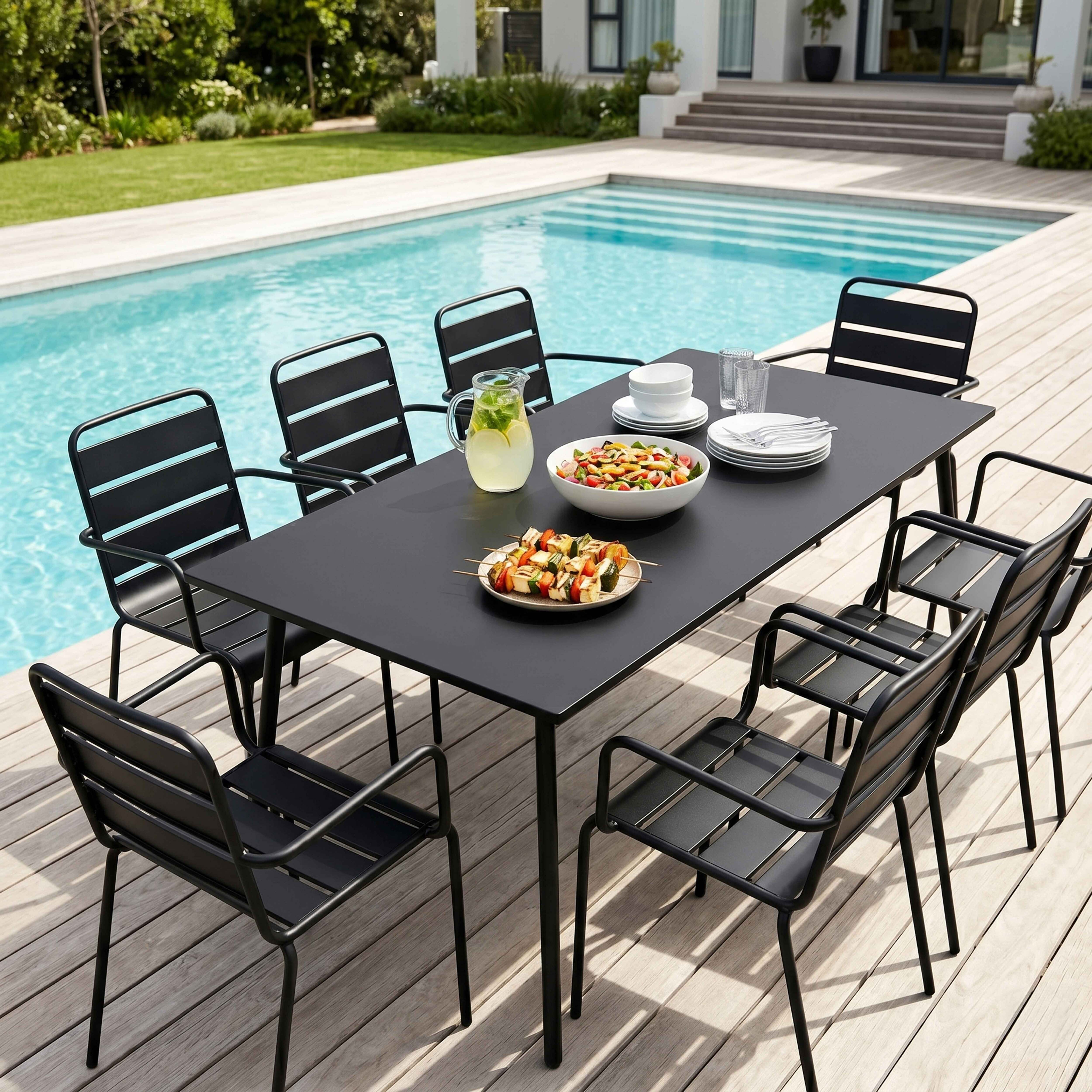 Schwarze Metalltisch- und Stuhl-Garnitur am blauen Pool mit Salat und Spießen.