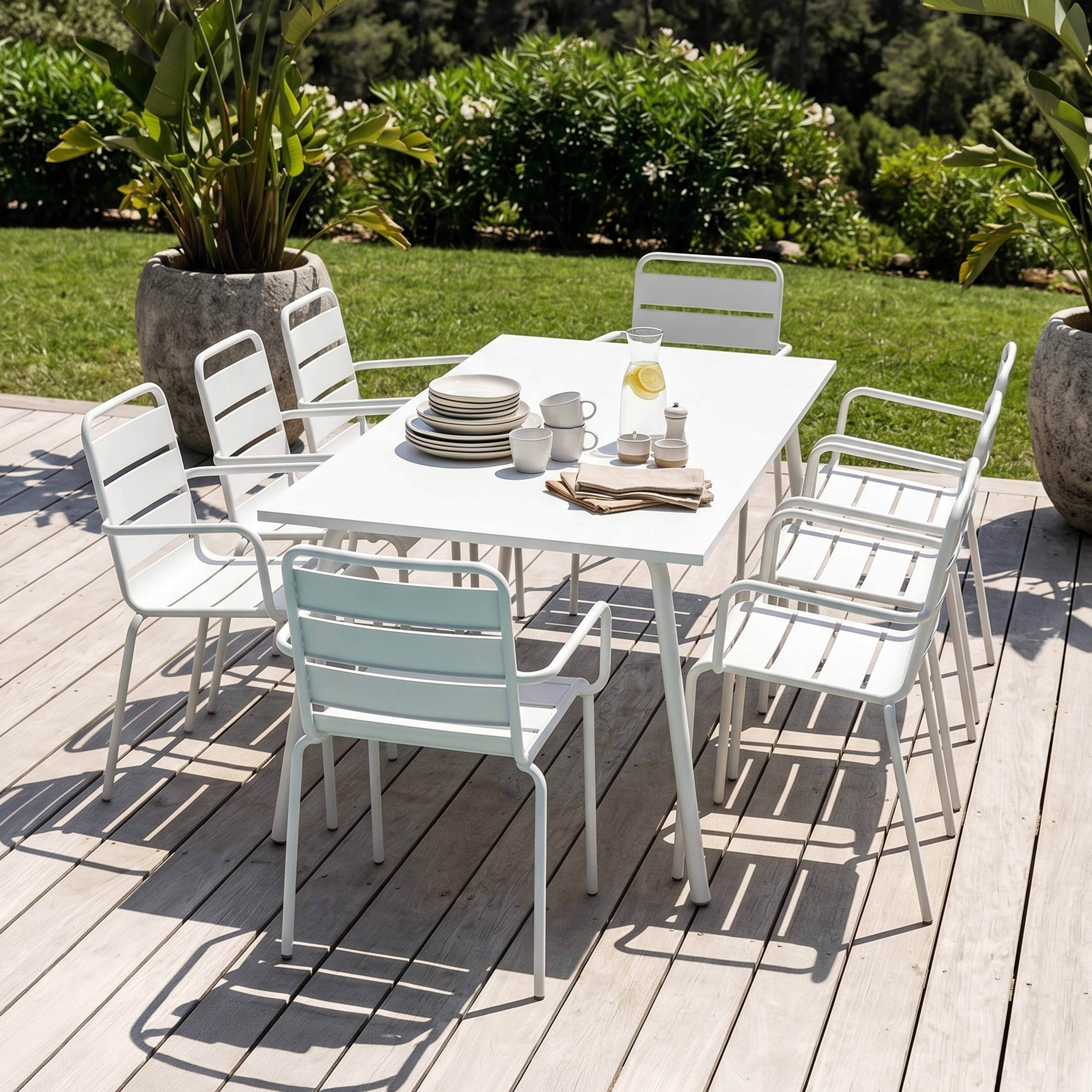 Weie Gartenmbel auf einer Holzterrasse mit Grnflche im Hintergrund.