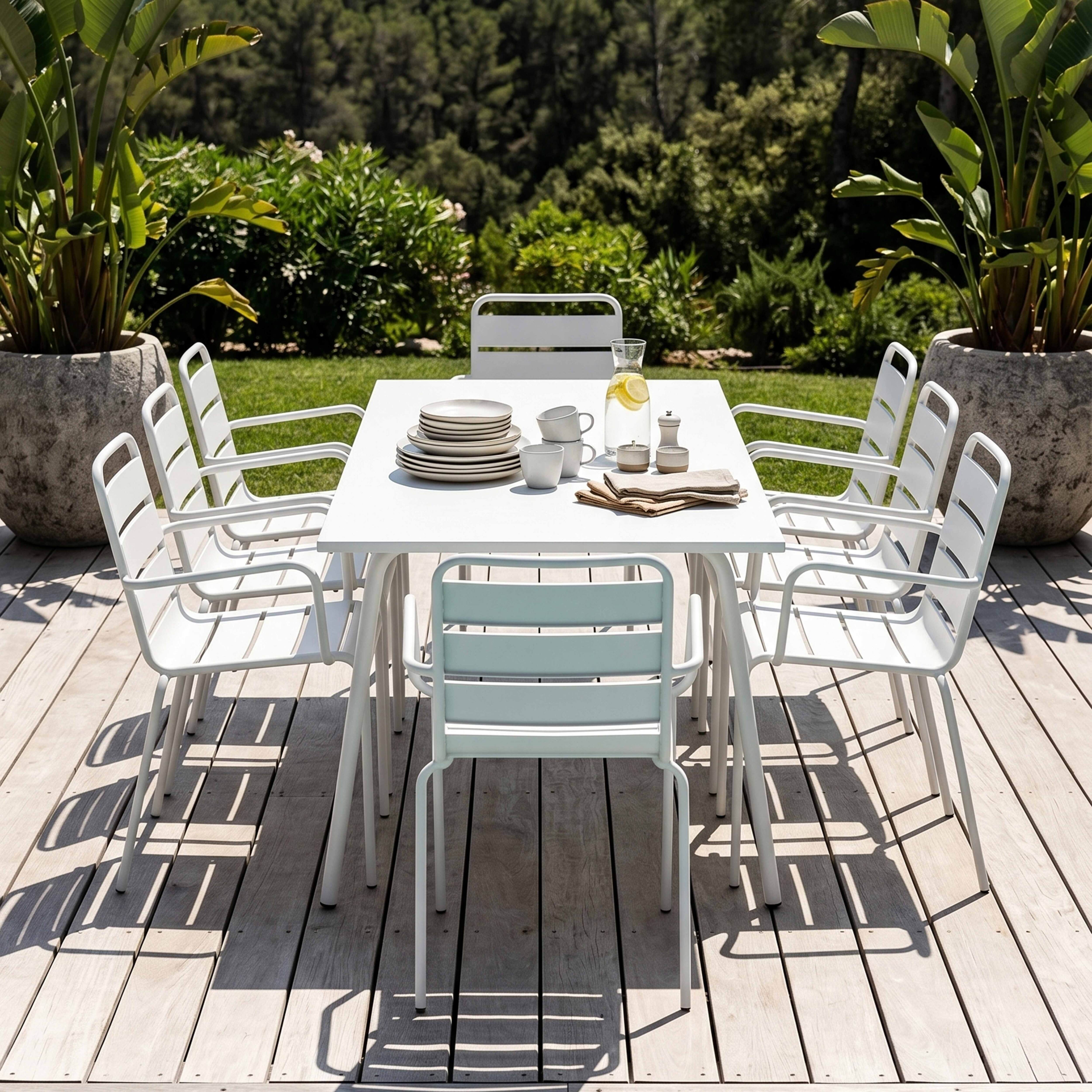 Weißes Gartentischset mit acht Stühlen auf Holzdeck, umgeben von grüner Vegetation.