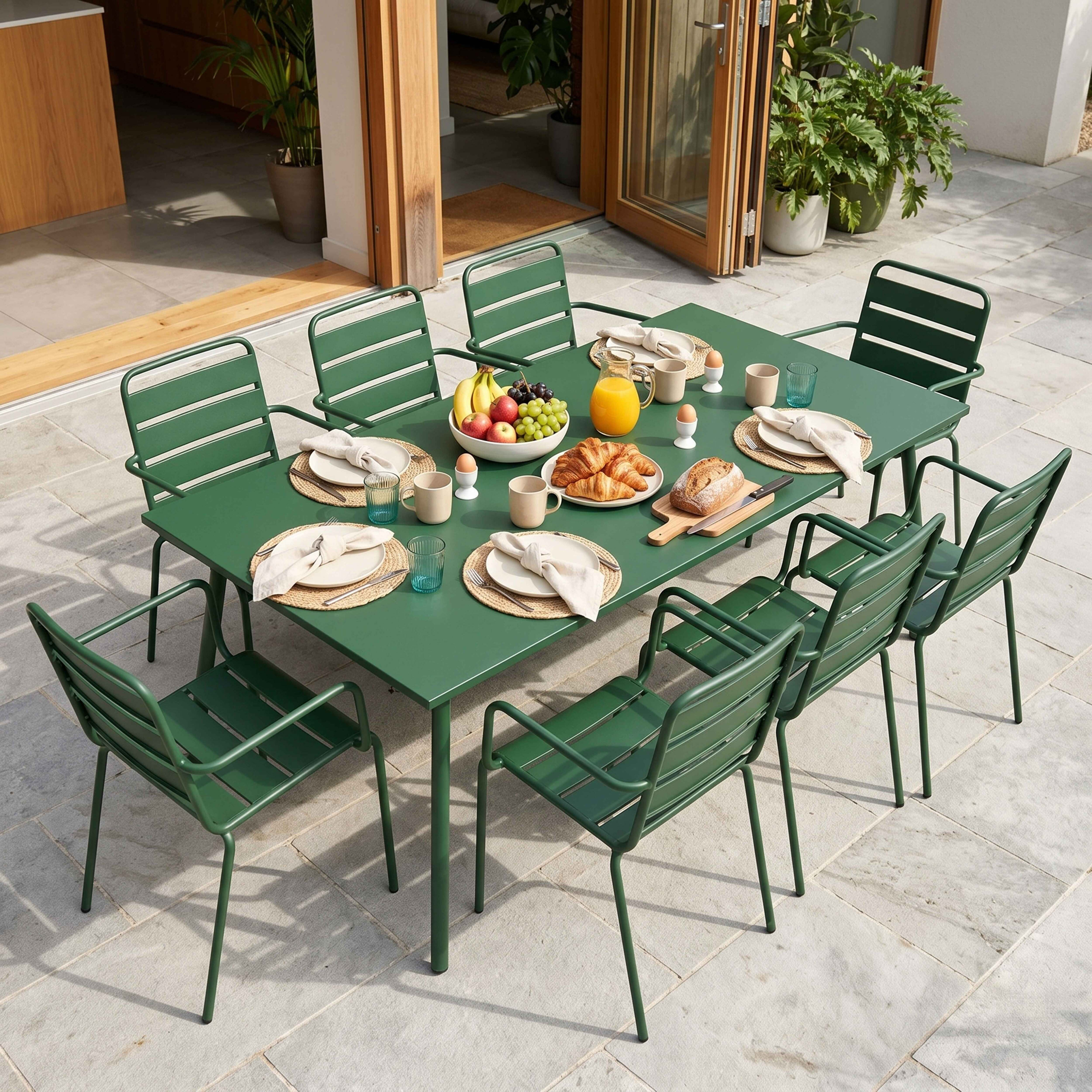 Grüner Gartentisch mit Frühstück, Croissants, Obst, Saft und Eiern, im Freien gedeckt.