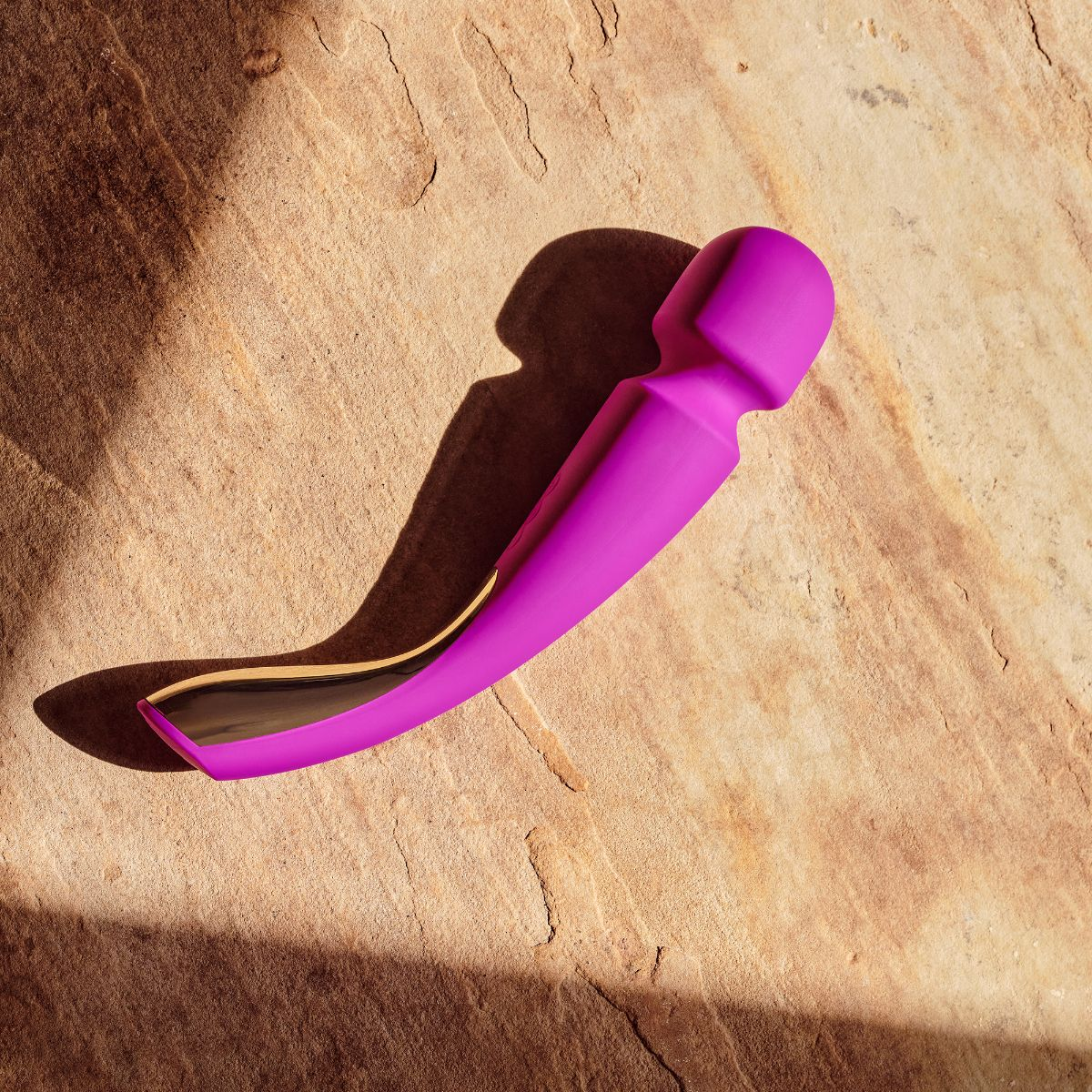 Lila Vibrator mit goldenem Akzent auf Stein mit Schatten.