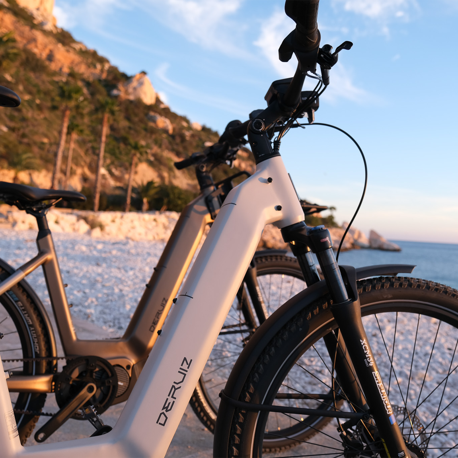 Zwei E-Bikes am Strand mit Bergen im Hintergrund bei Sonnenuntergang.
