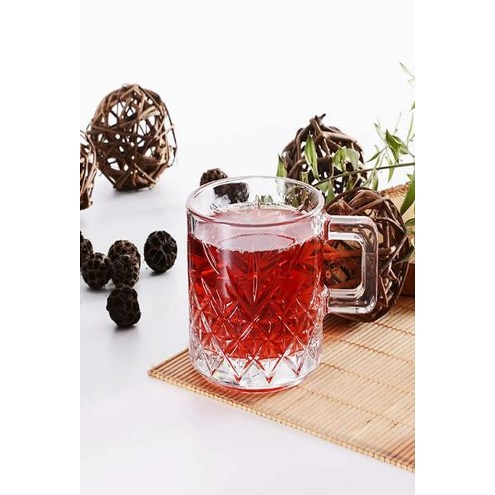 Bambu mat üzerinde dekoratif toplar ve bitkilerle dolu bir bardak kırmızı sıvı.