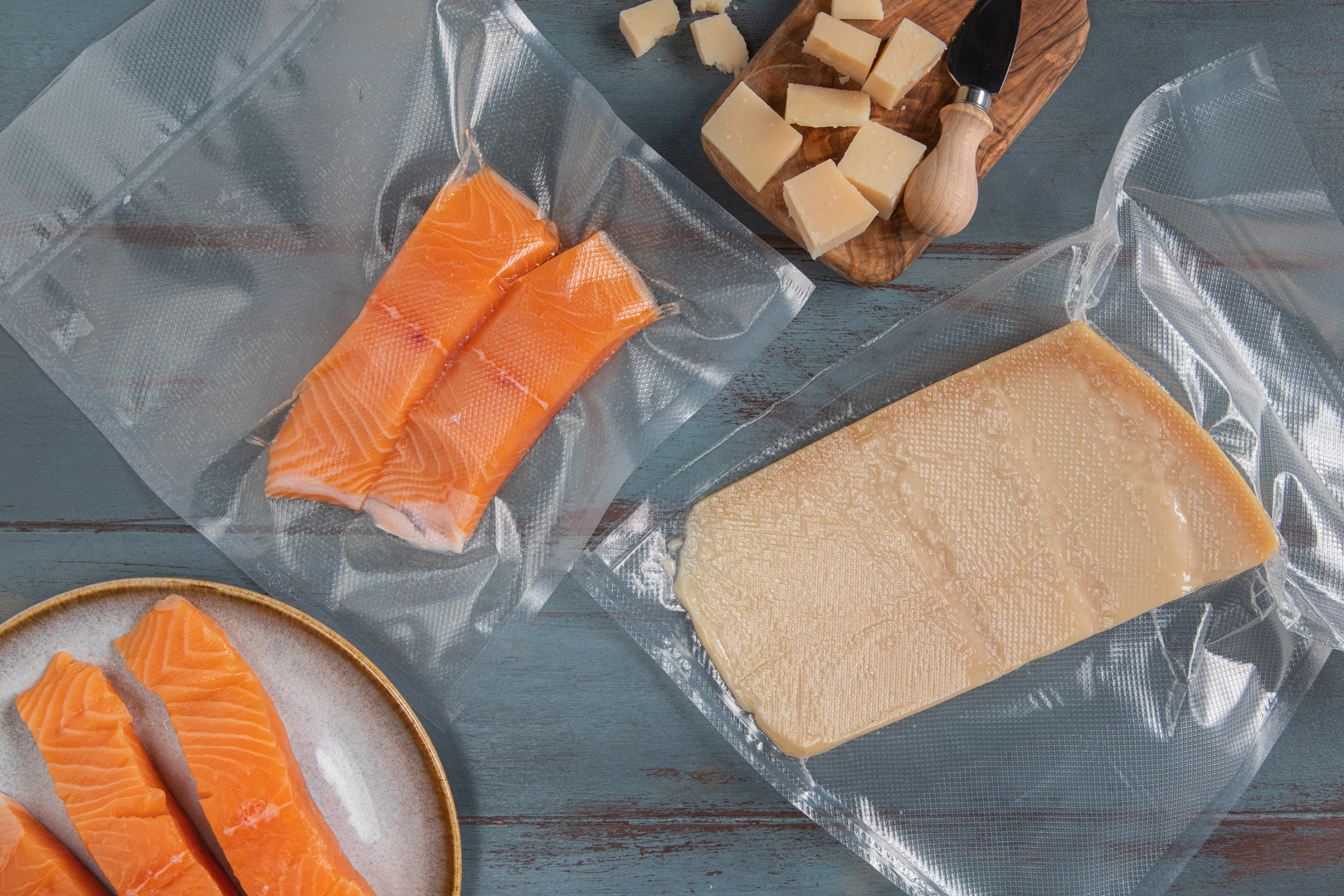 Salmón crudo en bolsas selladas al vacío y en un plato junto a un trozo de queso.