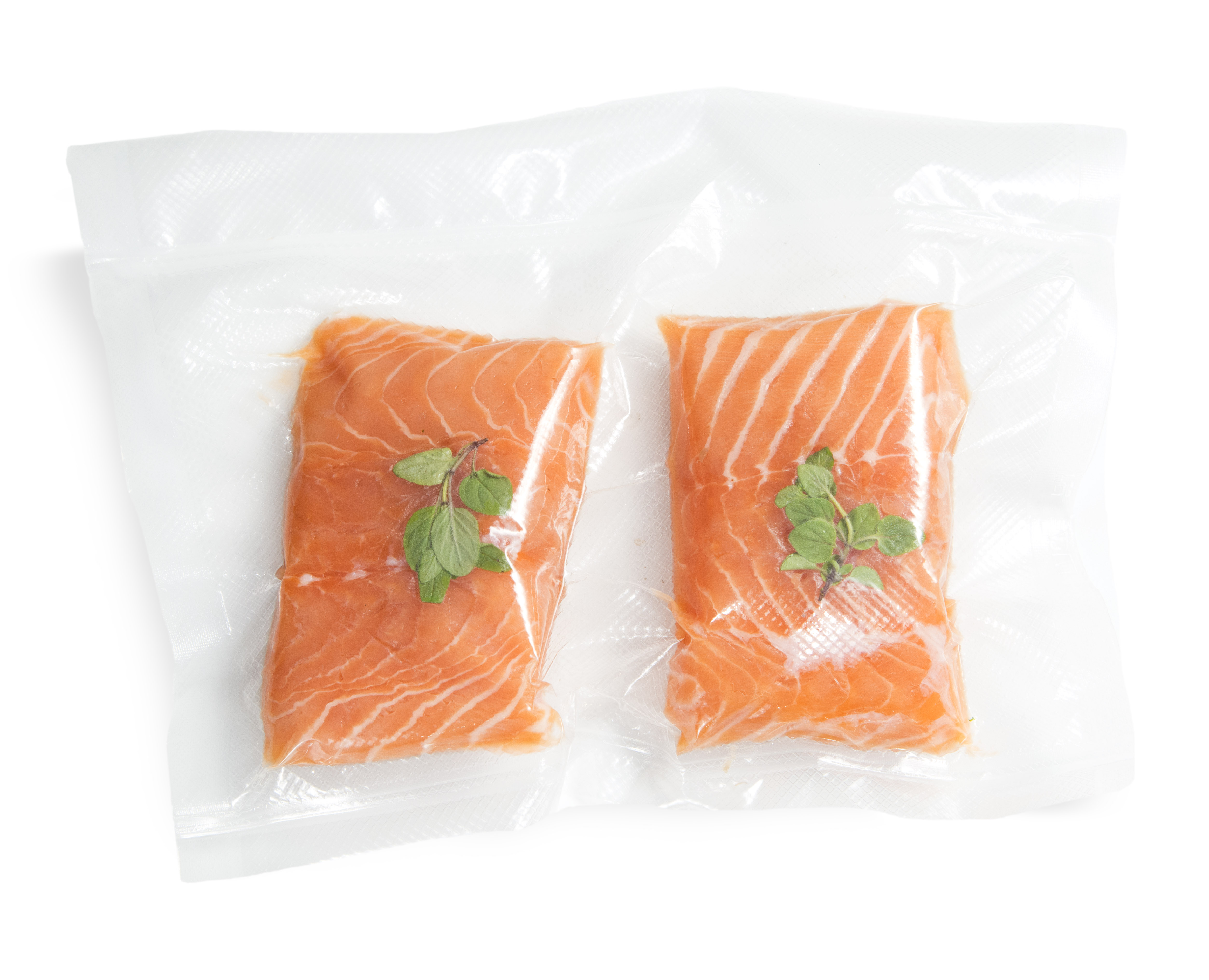 Dos filetes de salmón sellados al vacío con hierbas verdes sobre fondo blanco.