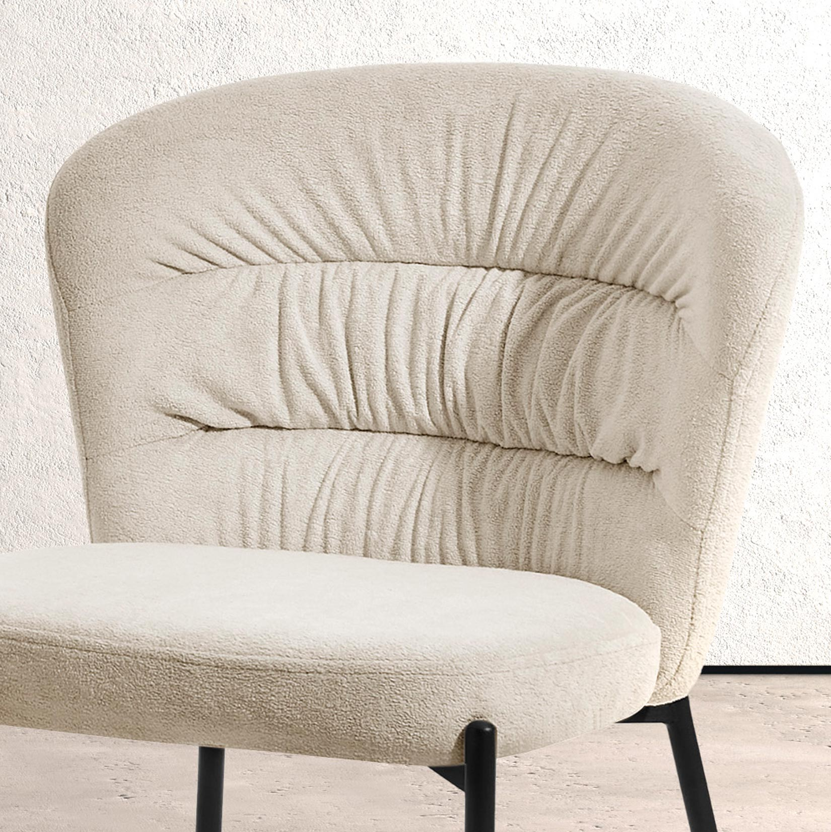 Un sillón color crema con respaldo fruncido y patas de metal negro.