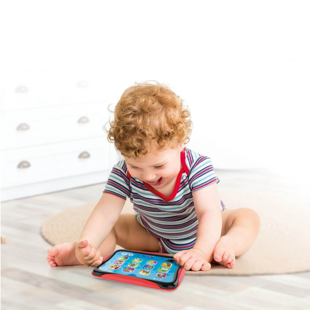 Un niño pequeño con pelo rizado y rojo juega con una tableta en el suelo.