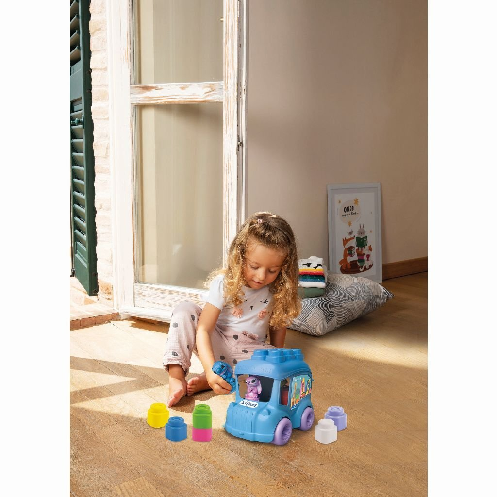 Una niña juega con un autobús de juguete azul y bloques de colores en un suelo de madera.