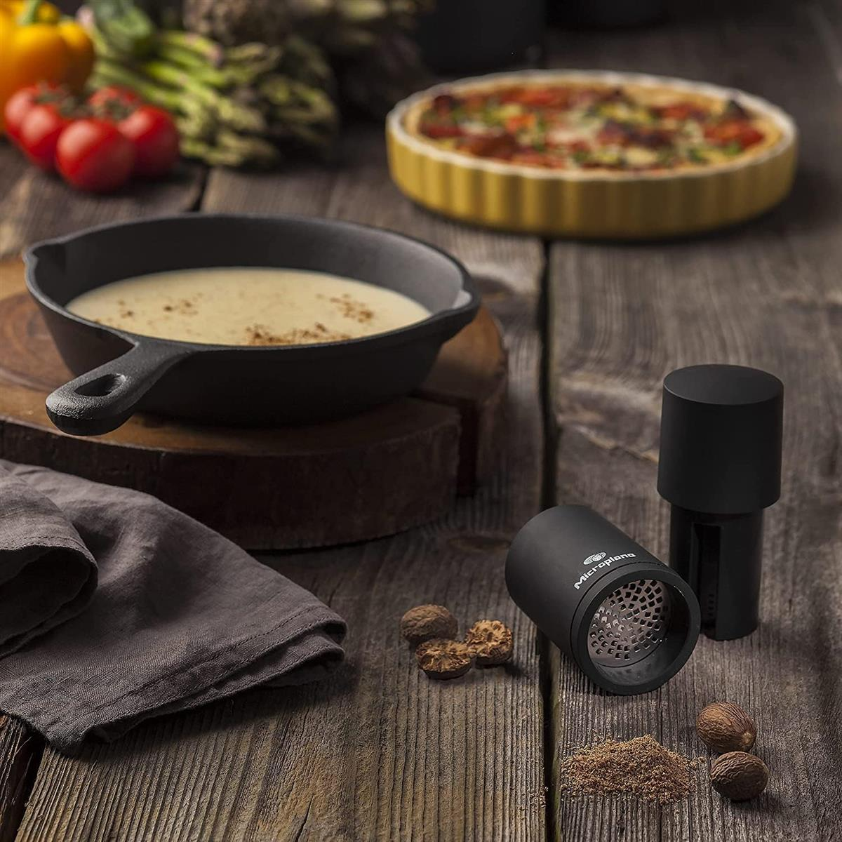Ein Kochtopf mit cremiger Suppe, Muskatnüsse und ein Reibe auf Holztisch.
