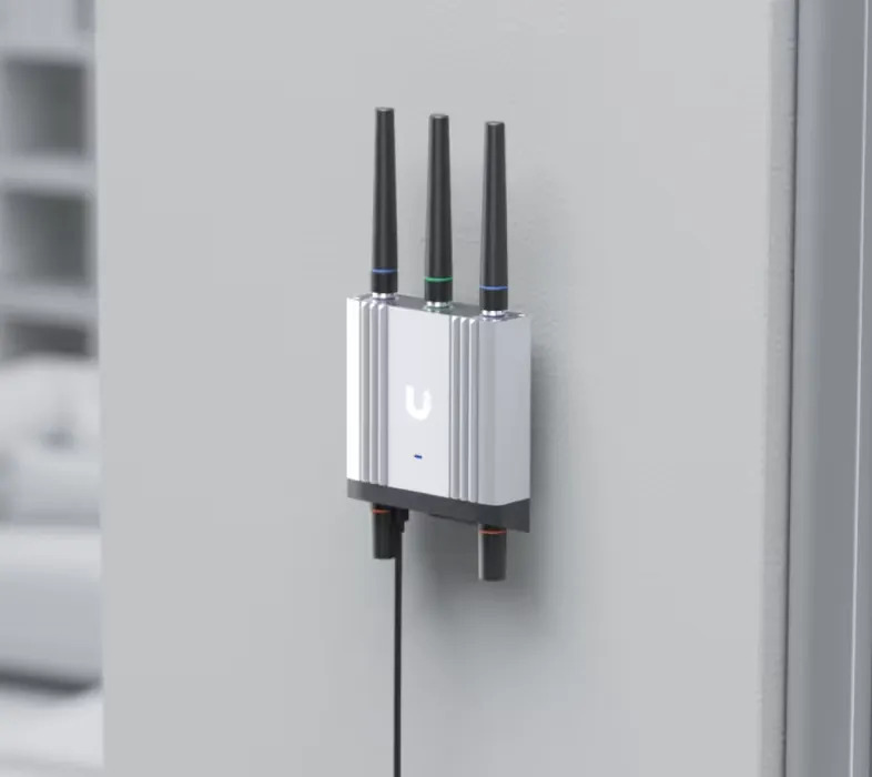 Un dispositivo argentato con tre antenne montato su un muro grigio.