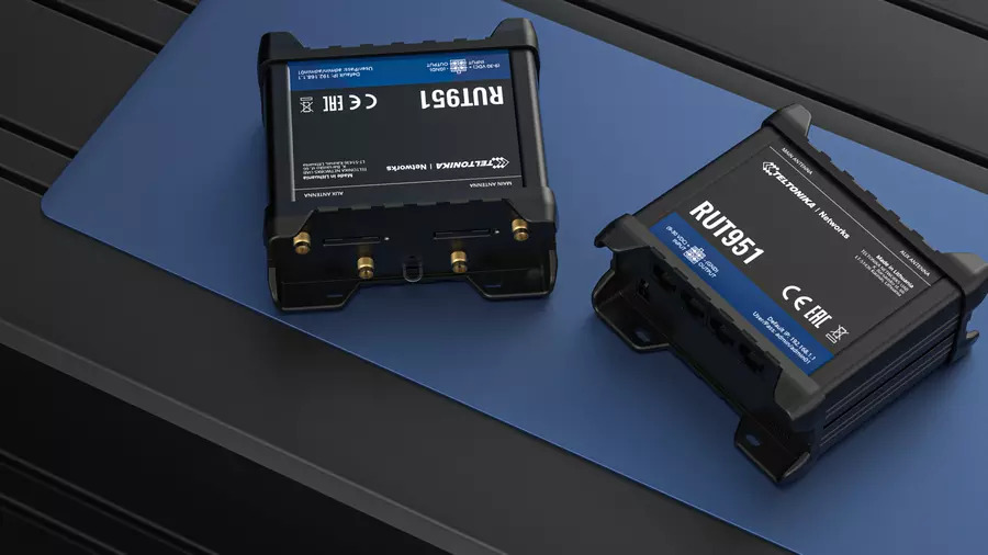 Two black Teltonika RUT951 routers with antennas on a blue mat.