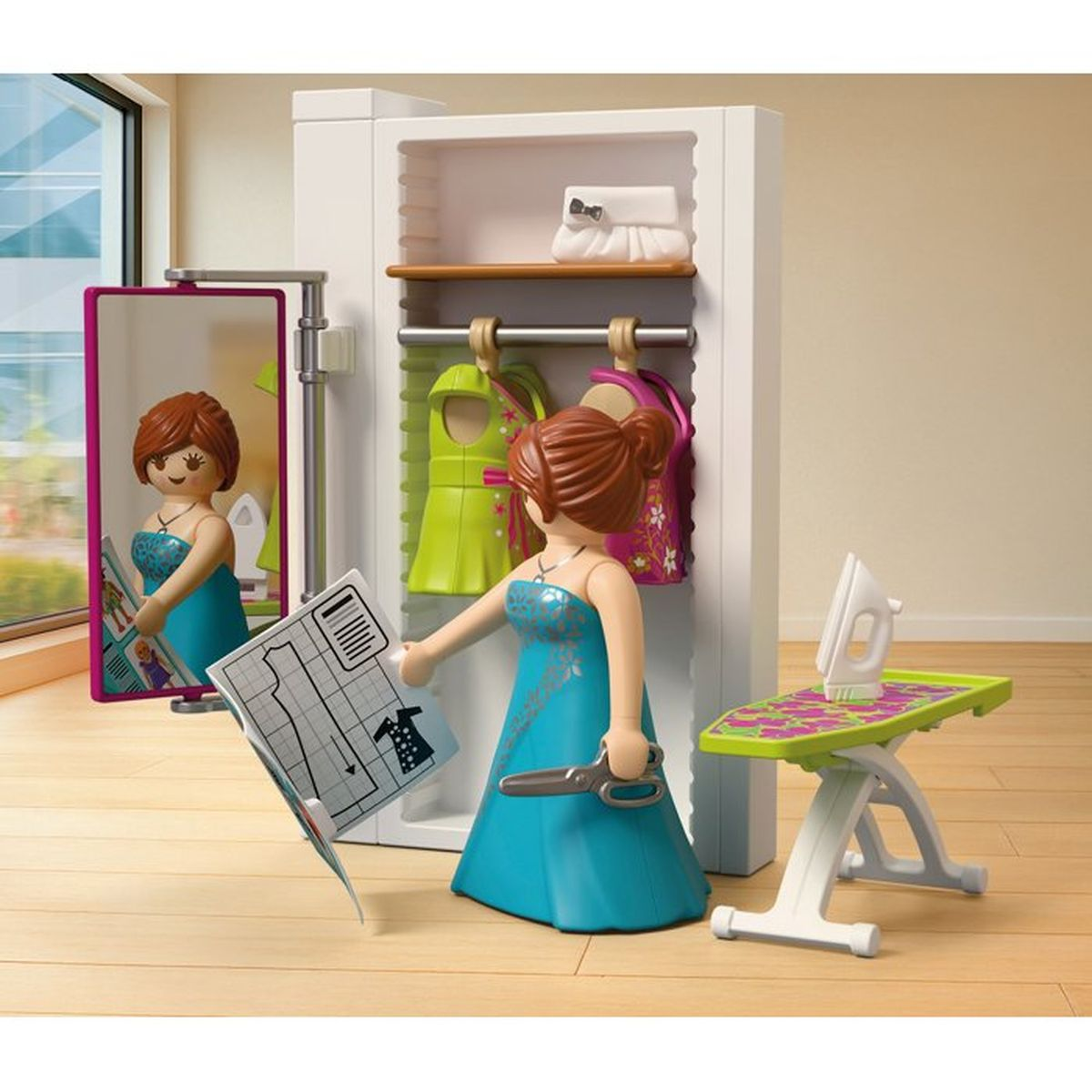 Figura Playmobil con vestido azul y tijeras, frente a armario con ropa, espejo y tabla de planchar.