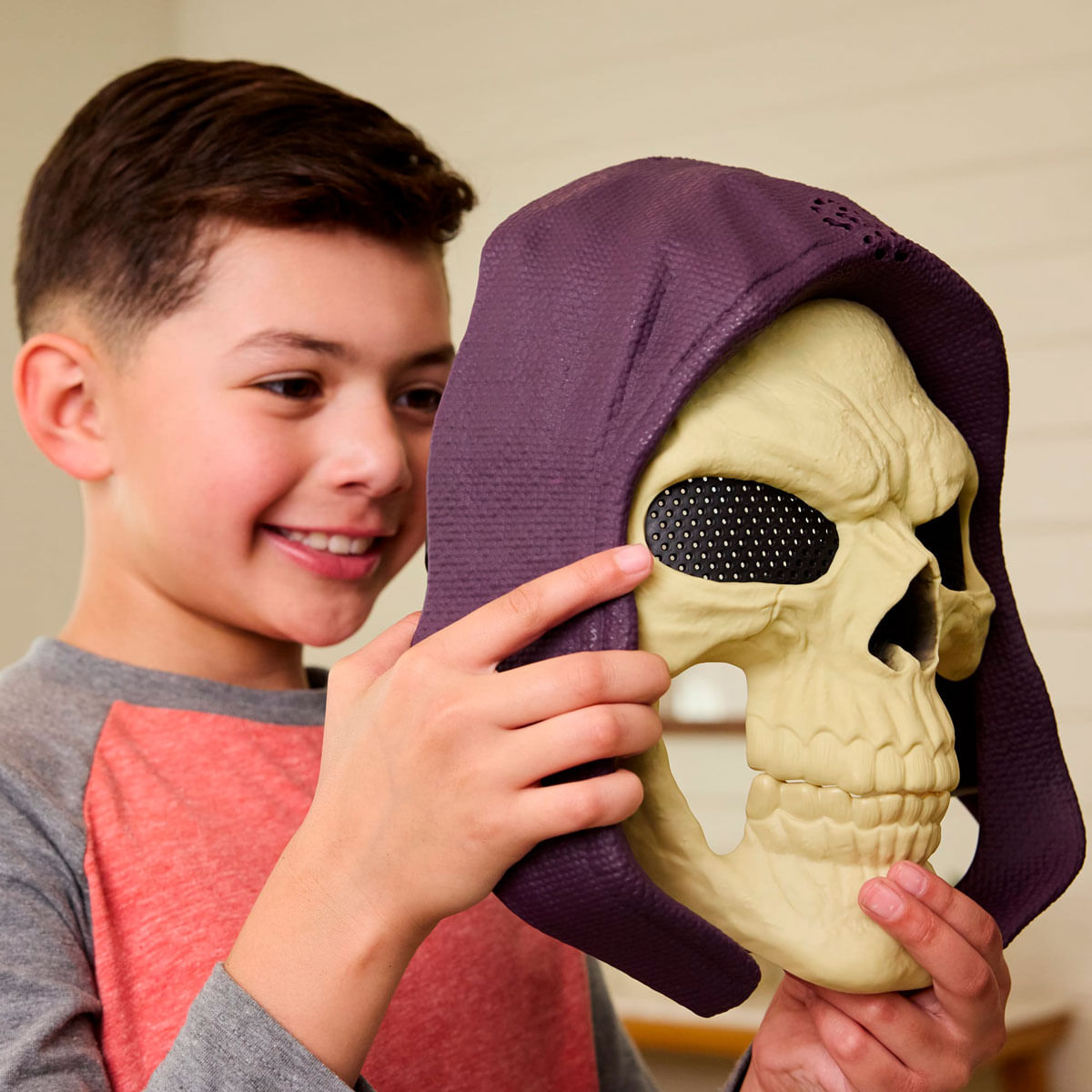 Un niño sujetando una máscara de calavera con capucha morada.