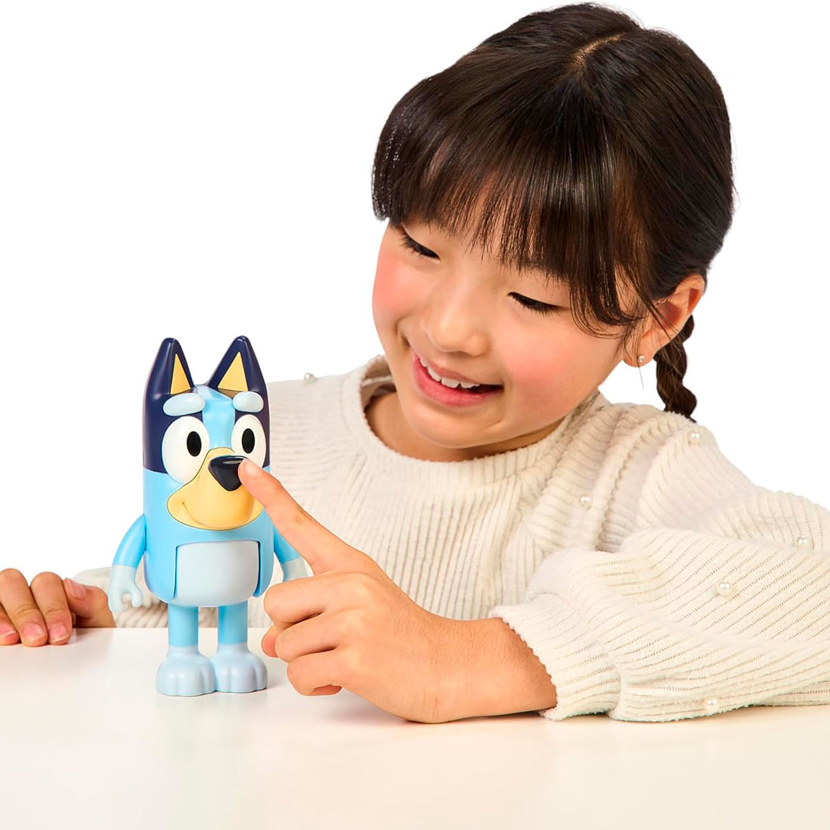 Una niña toca un juguete azul de Bluey con el dedo sobre una mesa blanca.