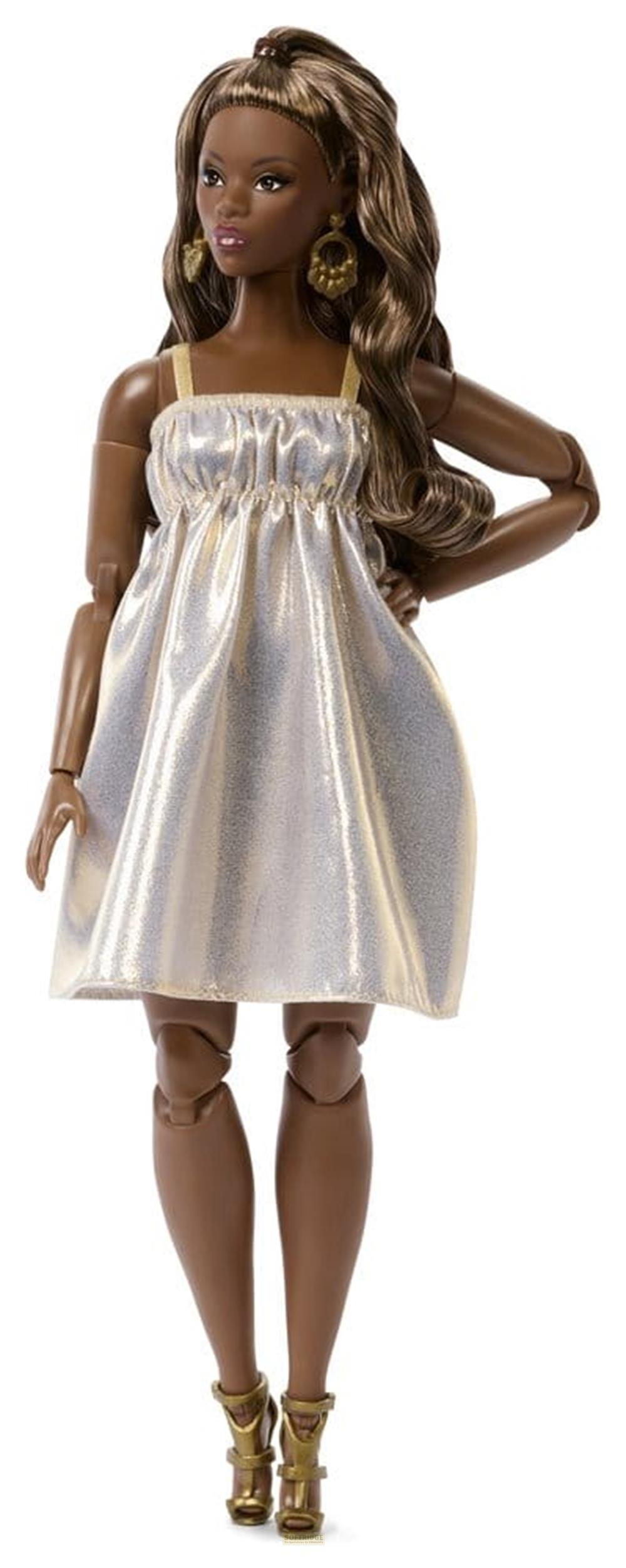 Una muñeca de moda con piel morena, cabello largo y ondulado y pendientes dorados lleva un vestido plateado brillante.