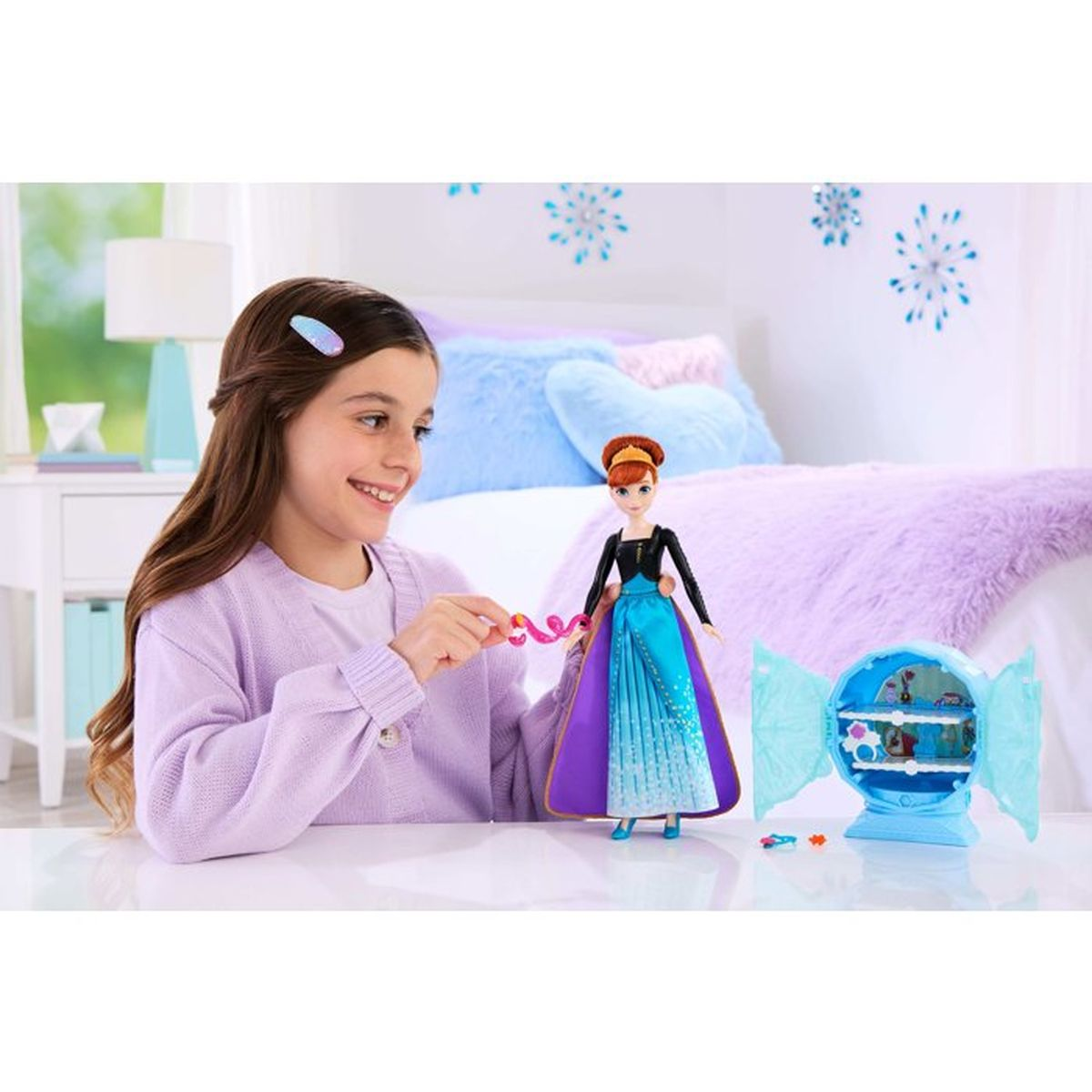 Una niña juega con una muñeca de Anna con vestido azul y morado. Un juguete con forma de caramelo está a su lado.