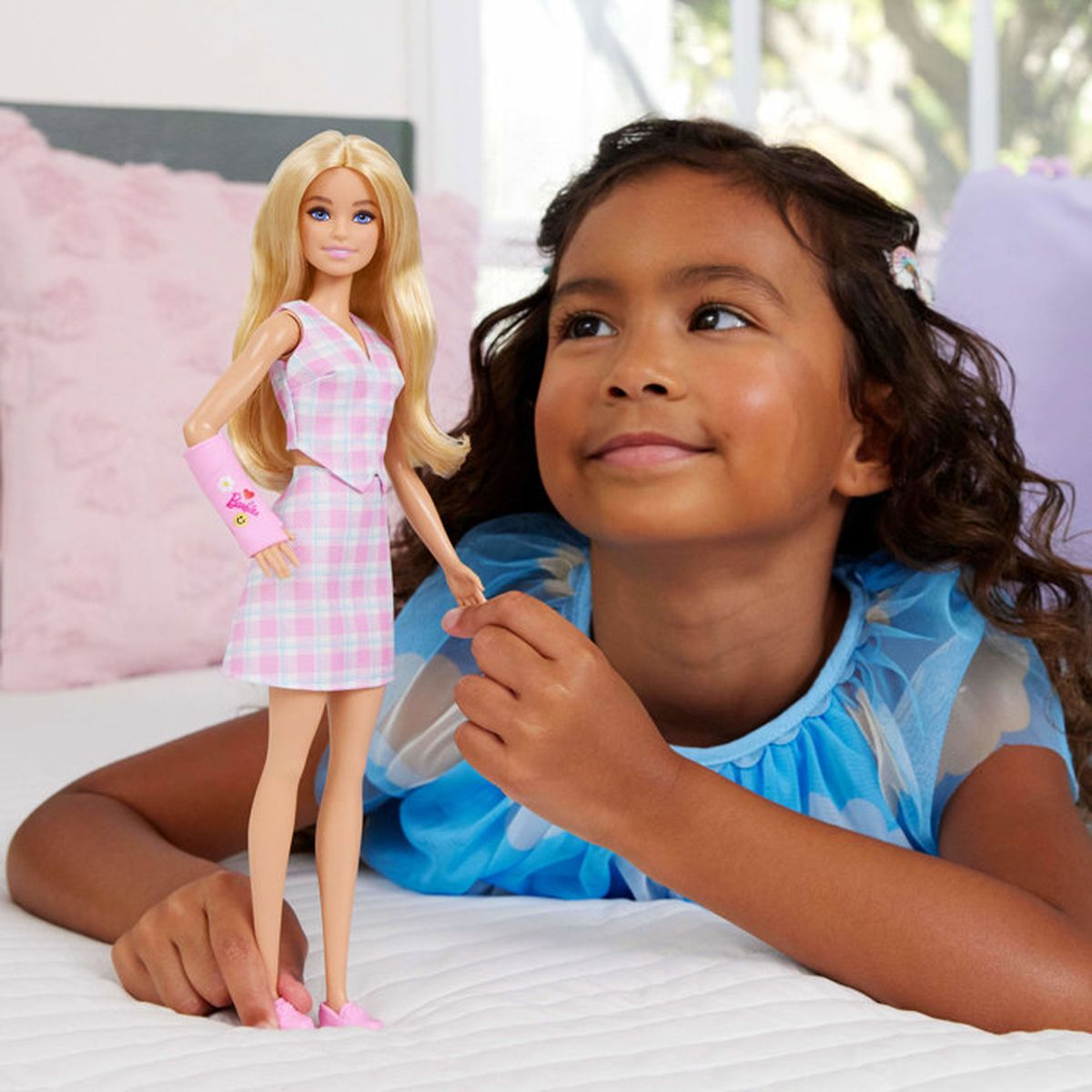 Una niña yace en una cama sosteniendo una muñeca Barbie con traje de cuadros rosa.