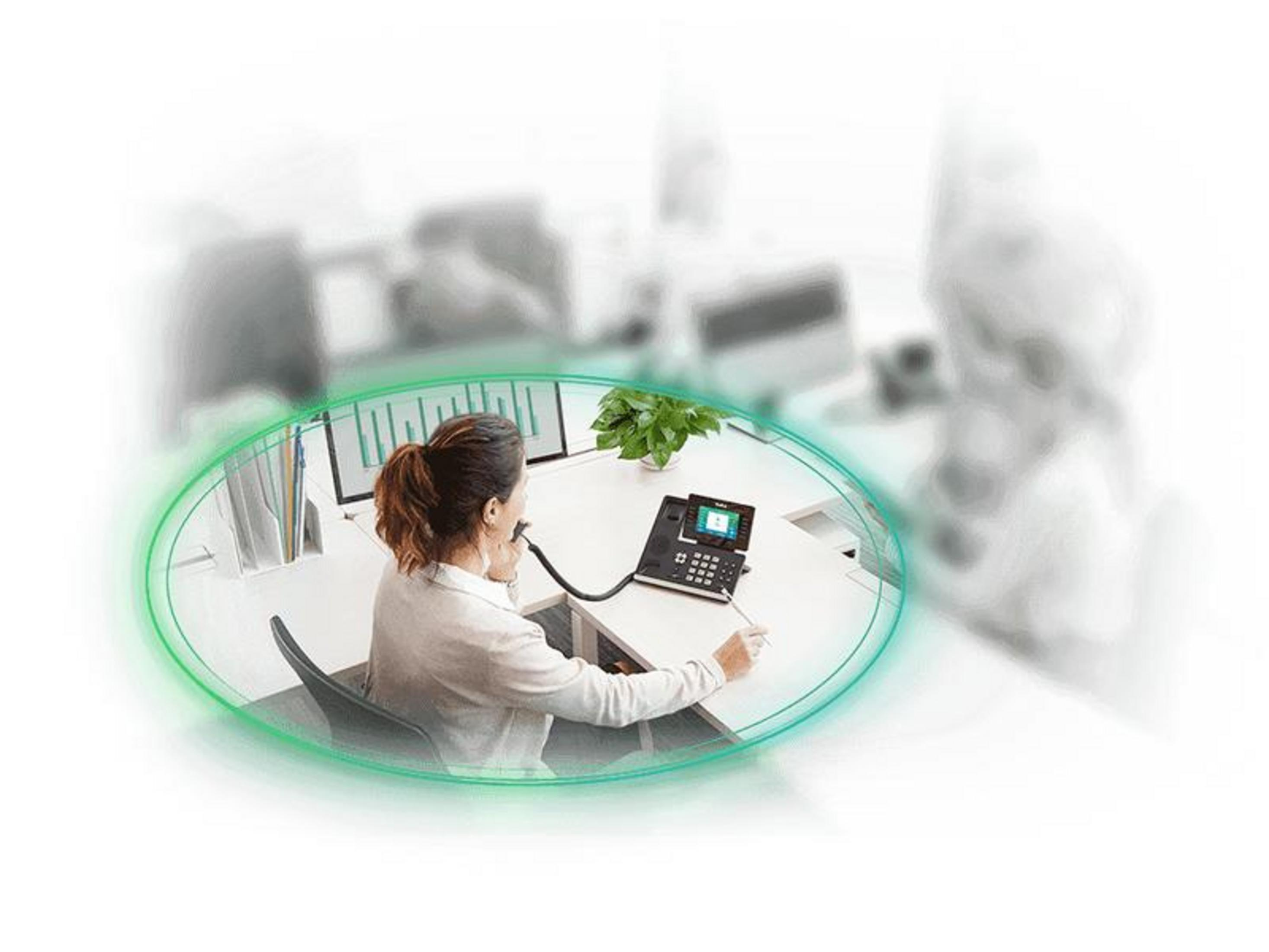 Mujer al teléfono en escritorio con monitores y planta.