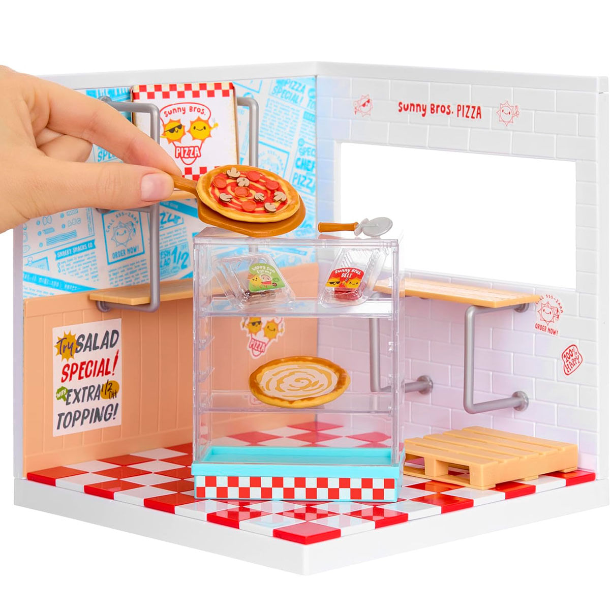 Una mano coloca una mini pizza en una pizzería de juguete con suelo a cuadros.