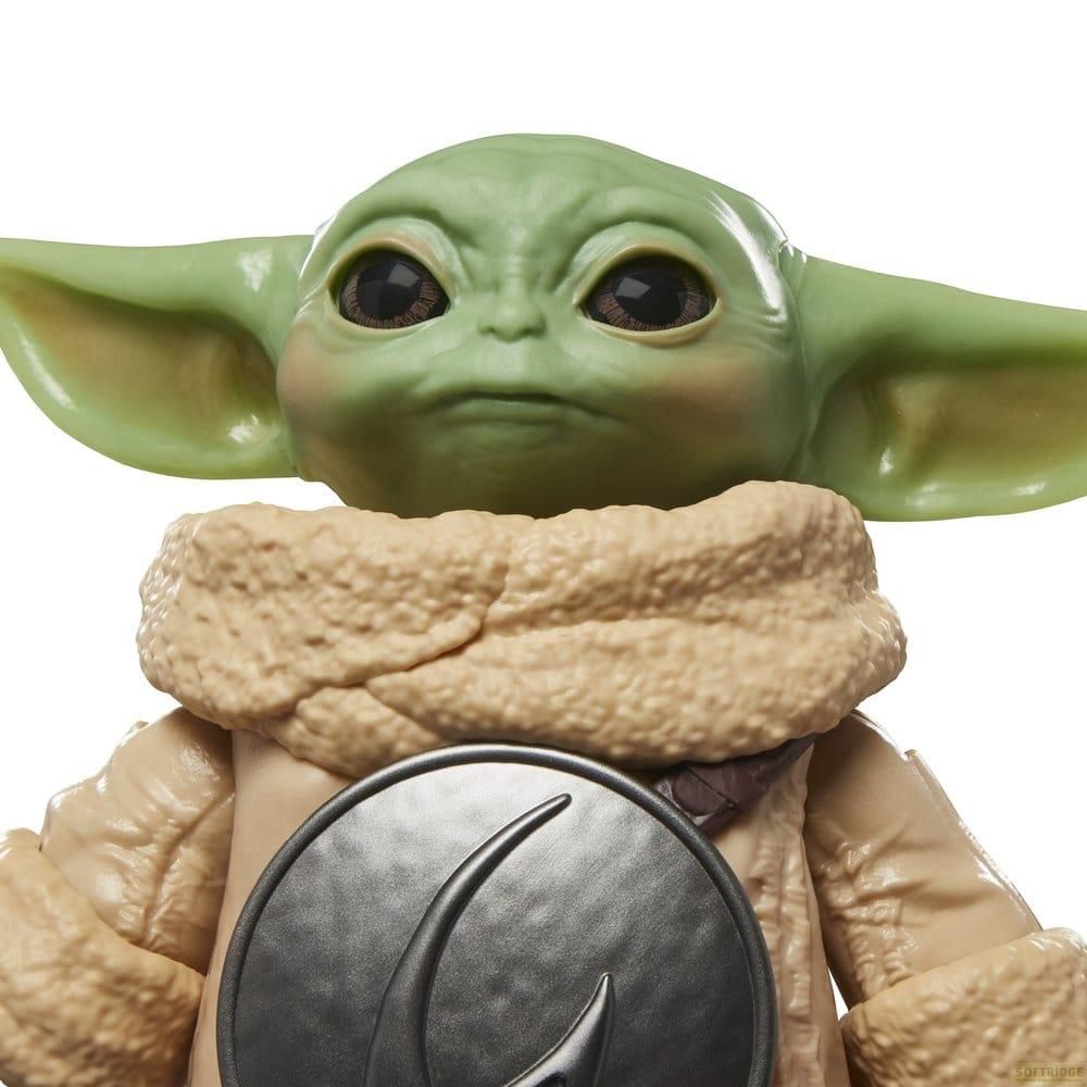 Figura de Baby Yoda con túnica beige y emblema plateado.