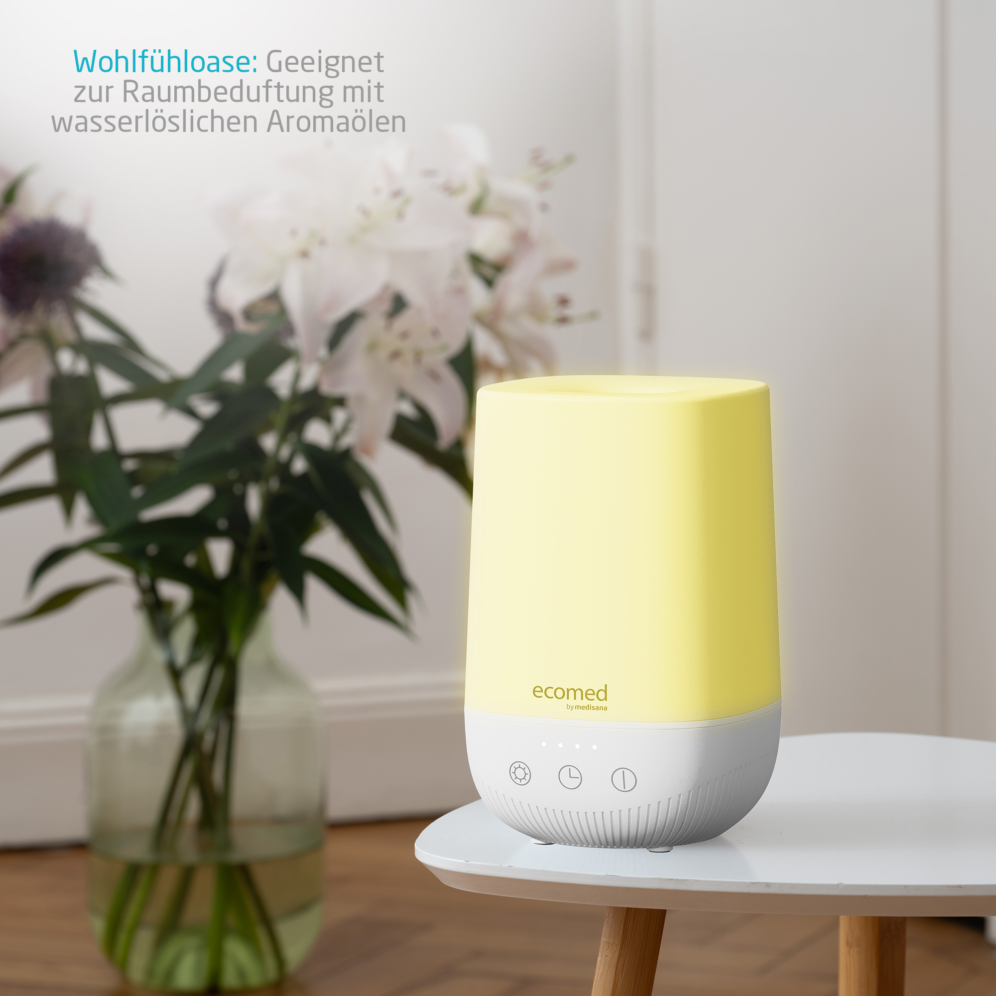 Ein gelber Diffusor mit Touch-Bedienelementen steht auf einem Tisch neben Blumen.