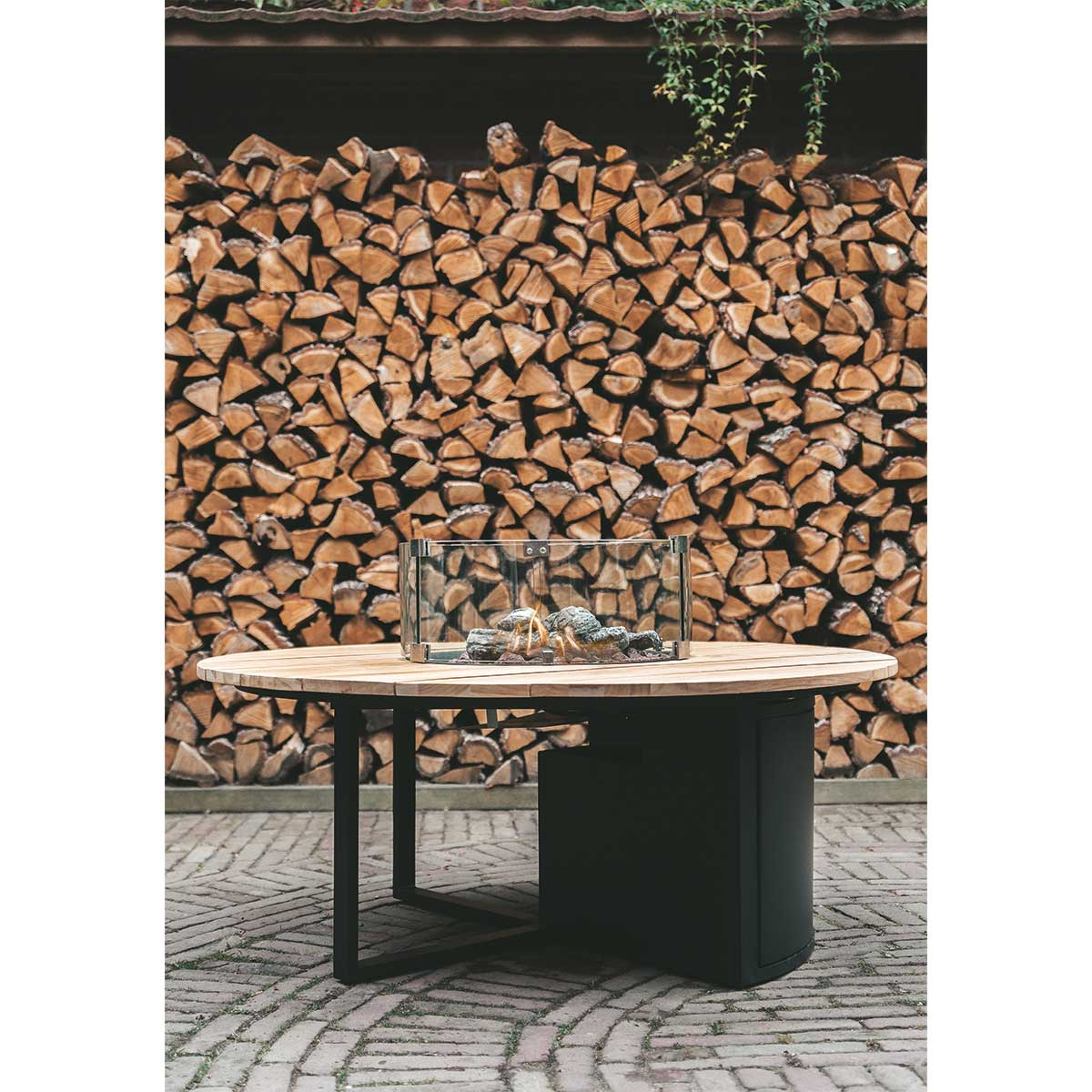 Table ronde en bois avec foyer vitré, devant un mur de bois empilé.