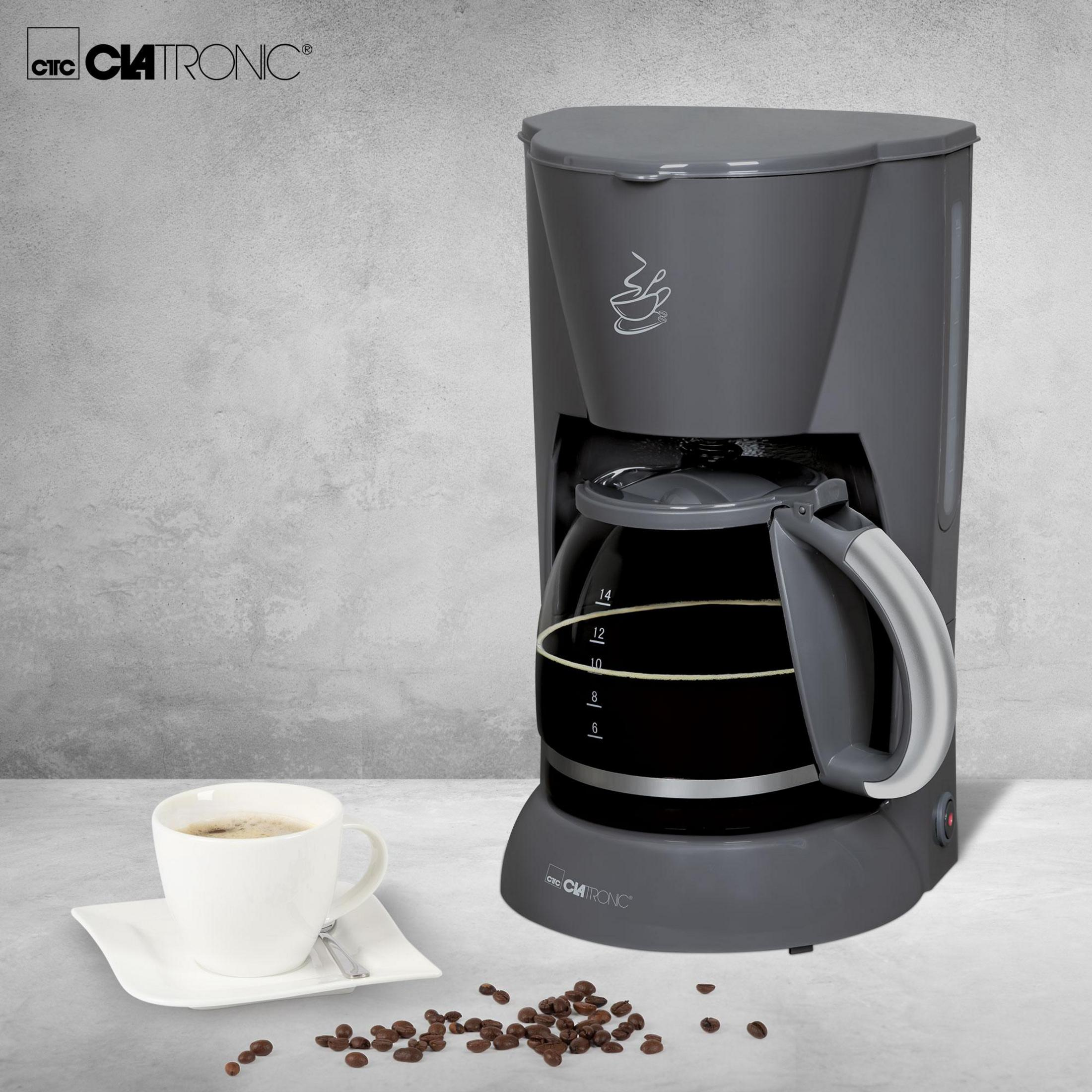 Cafetera gris CLATRONIC con jarra de vidrio, taza de café y granos.