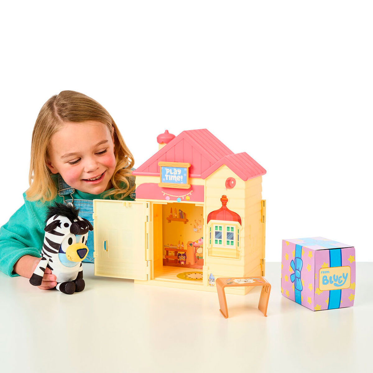 Una niña juega con una casa de juguete de Bluey, un peluche de cebra y una caja de regalo.