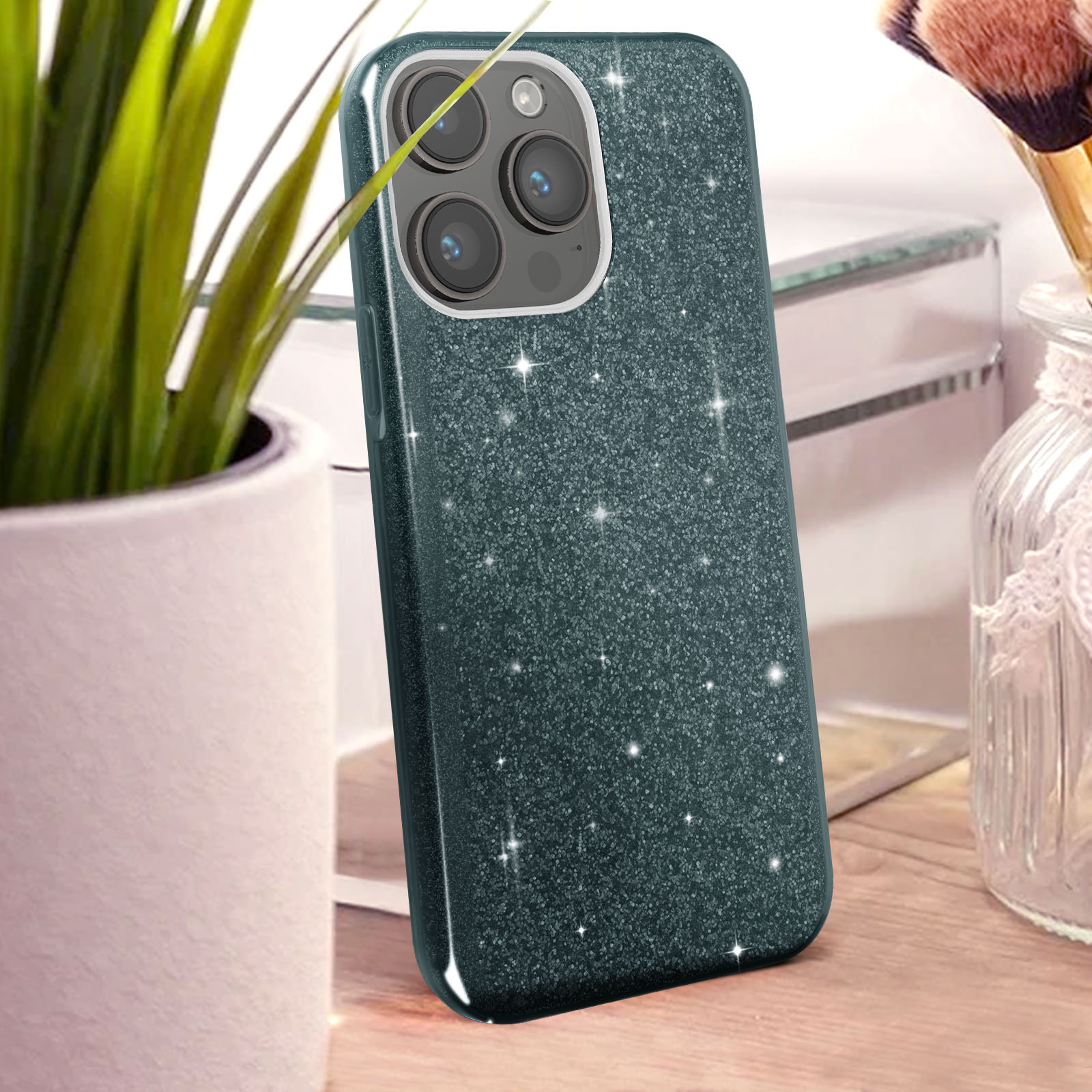 Custodia per telefono glitter verde acqua scuro con array fotocamera, vicino a pianta e pennello.