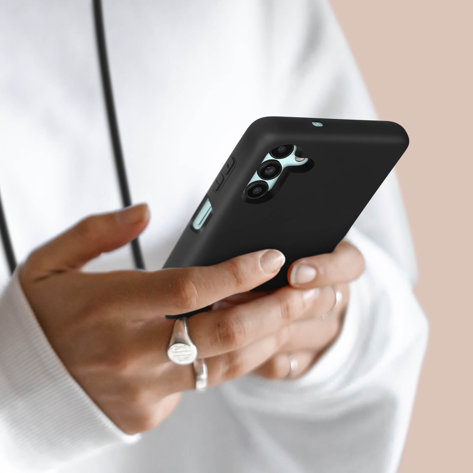 Persona che tiene uno smartphone nero con fotocamere su sfondo chiaro.