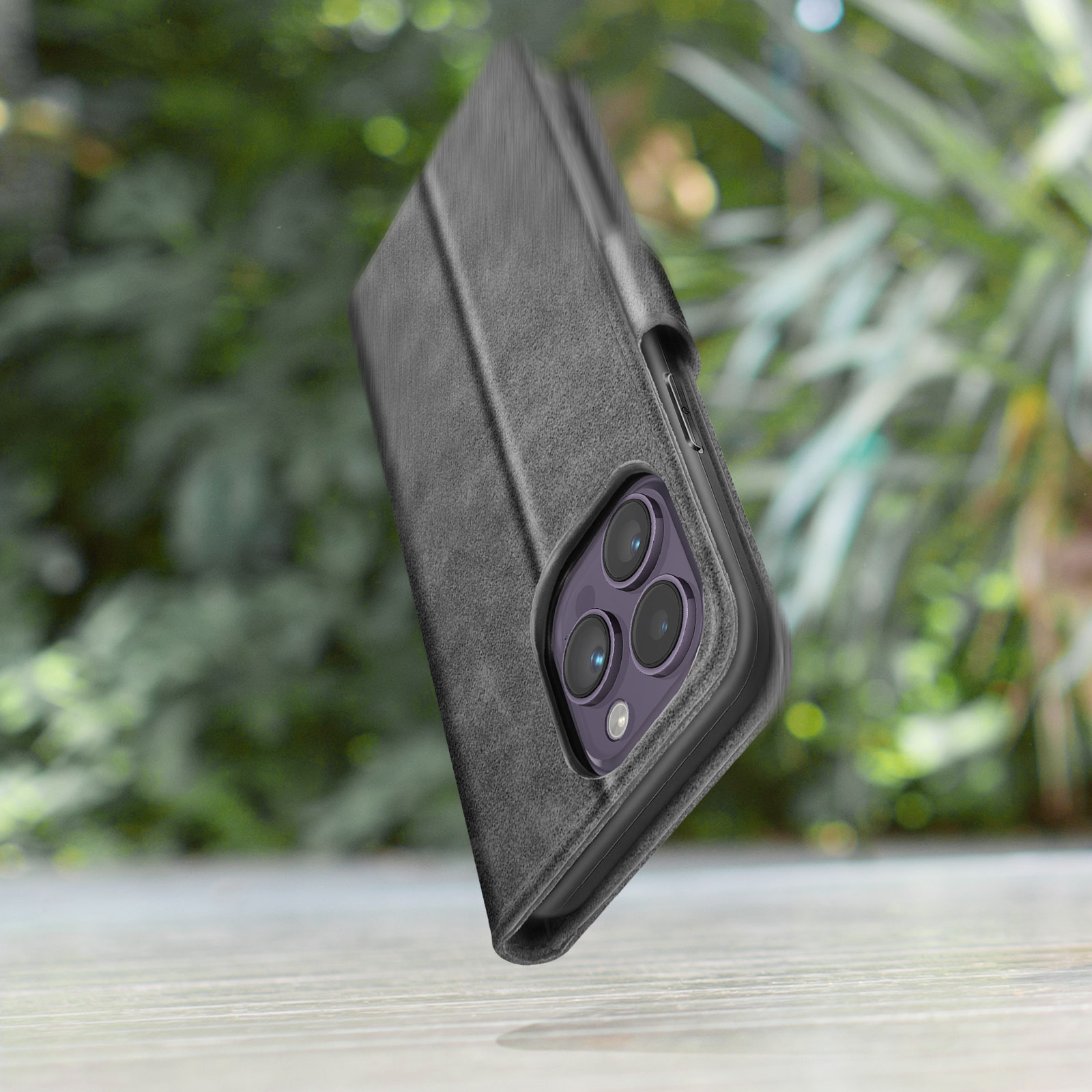 Graues Handy-Flipcase mit Kameras auf Holztisch vor Bäumen.