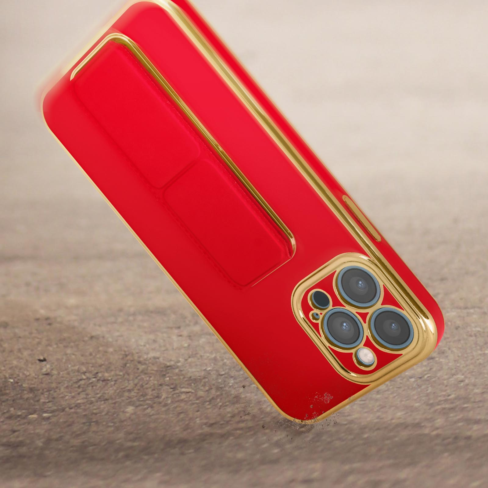 Una custodia per telefono rossa con finiture dorate poggia su una superficie ruvida. Ha una matrice di fotocamere.