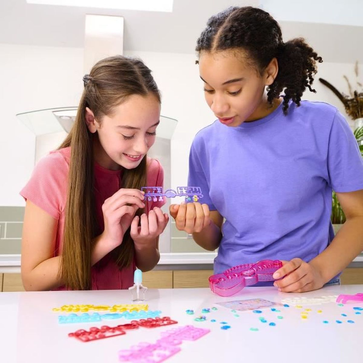 Dos niñas hacen pulseras de cuentas coloridas en una mesa blanca.