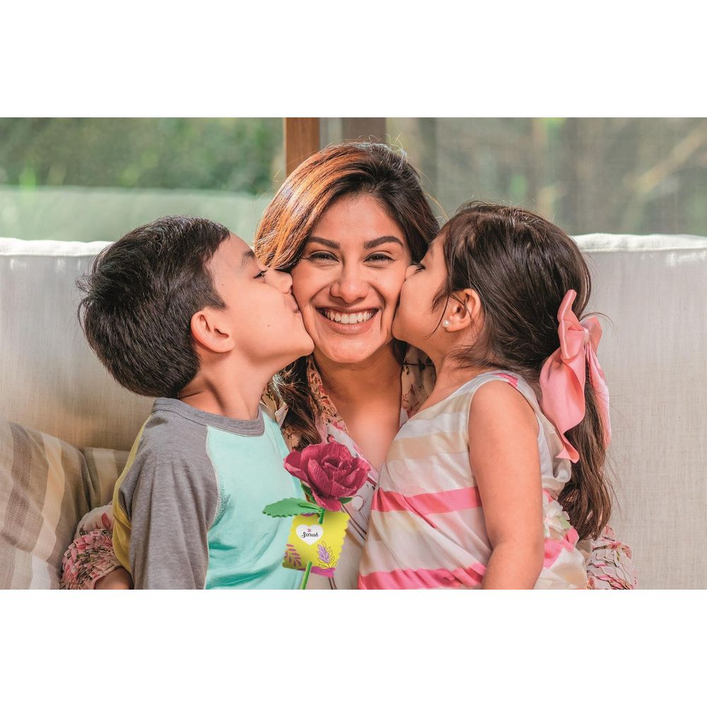 Madre y dos niños la besan en las mejillas, ella sostiene una flor.