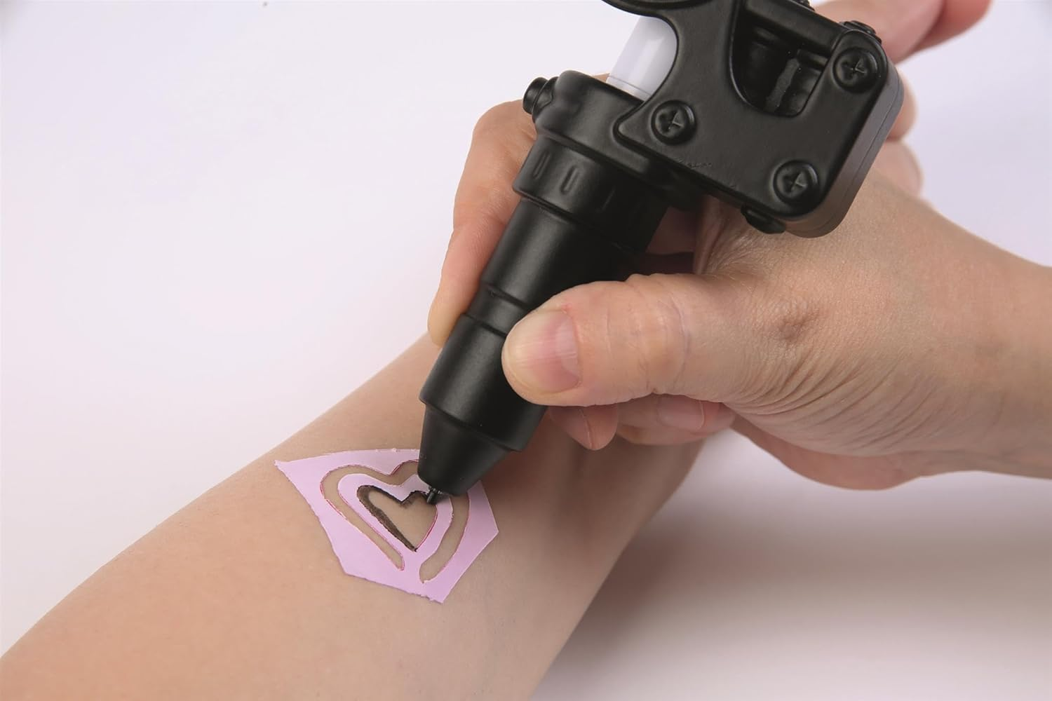 Mano usando una herramienta negra para aplicar una plantilla de corazón en un brazo.