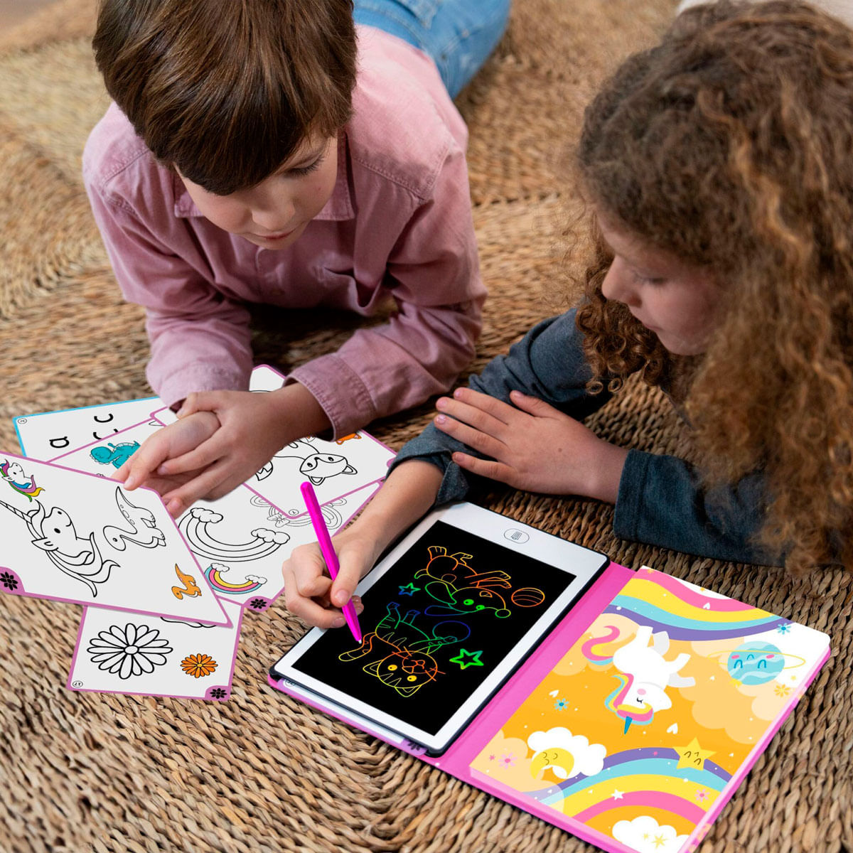 Dos niños tumbados en una alfombra dibujan en una tablet digital y en papel.