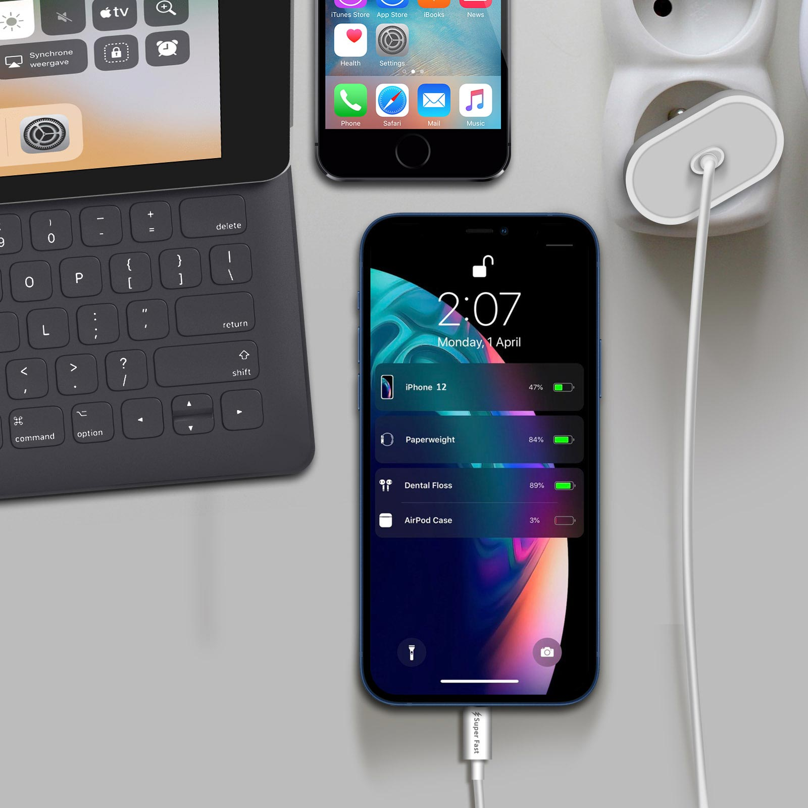 Ein iPhone 12 mit geringem Akkustand wird neben einer Tastatur und einem anderen Telefon geladen.