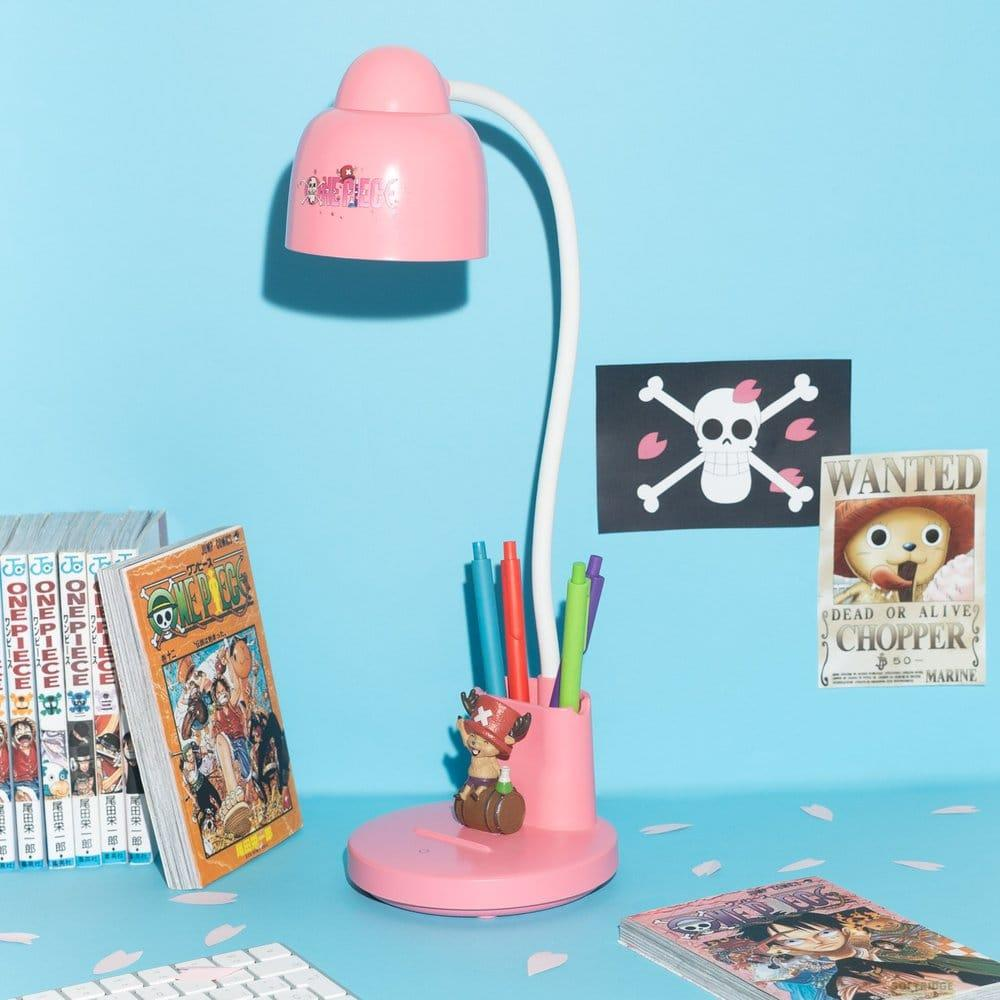 Un portalápices de lámpara de escritorio rosa con bolígrafos, manga de One Piece y pósters.