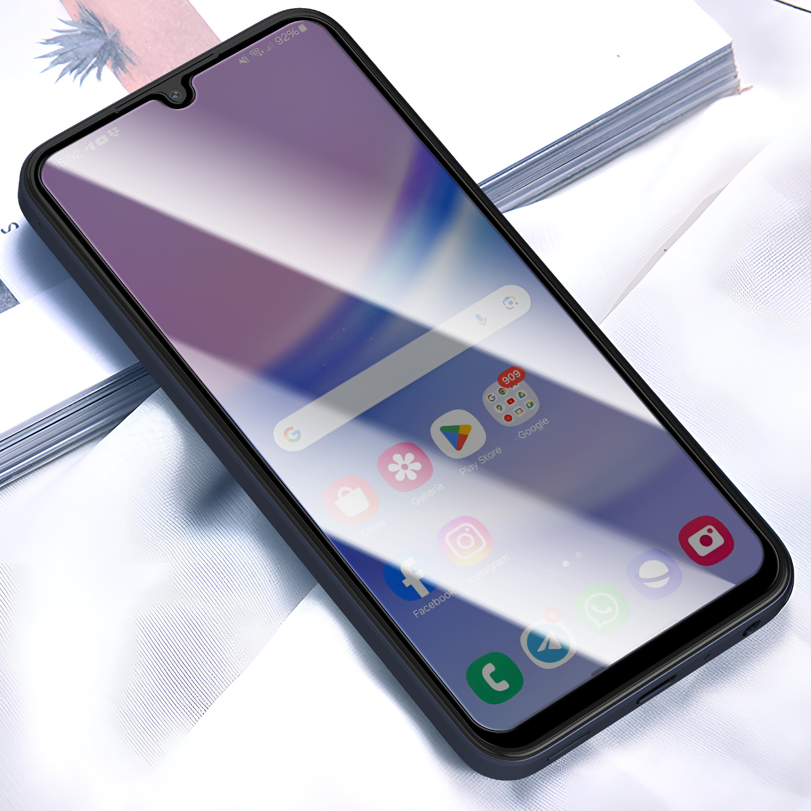 Uno smartphone nero con schermo viola mostra icone di app, appoggiato su tessuto bianco.